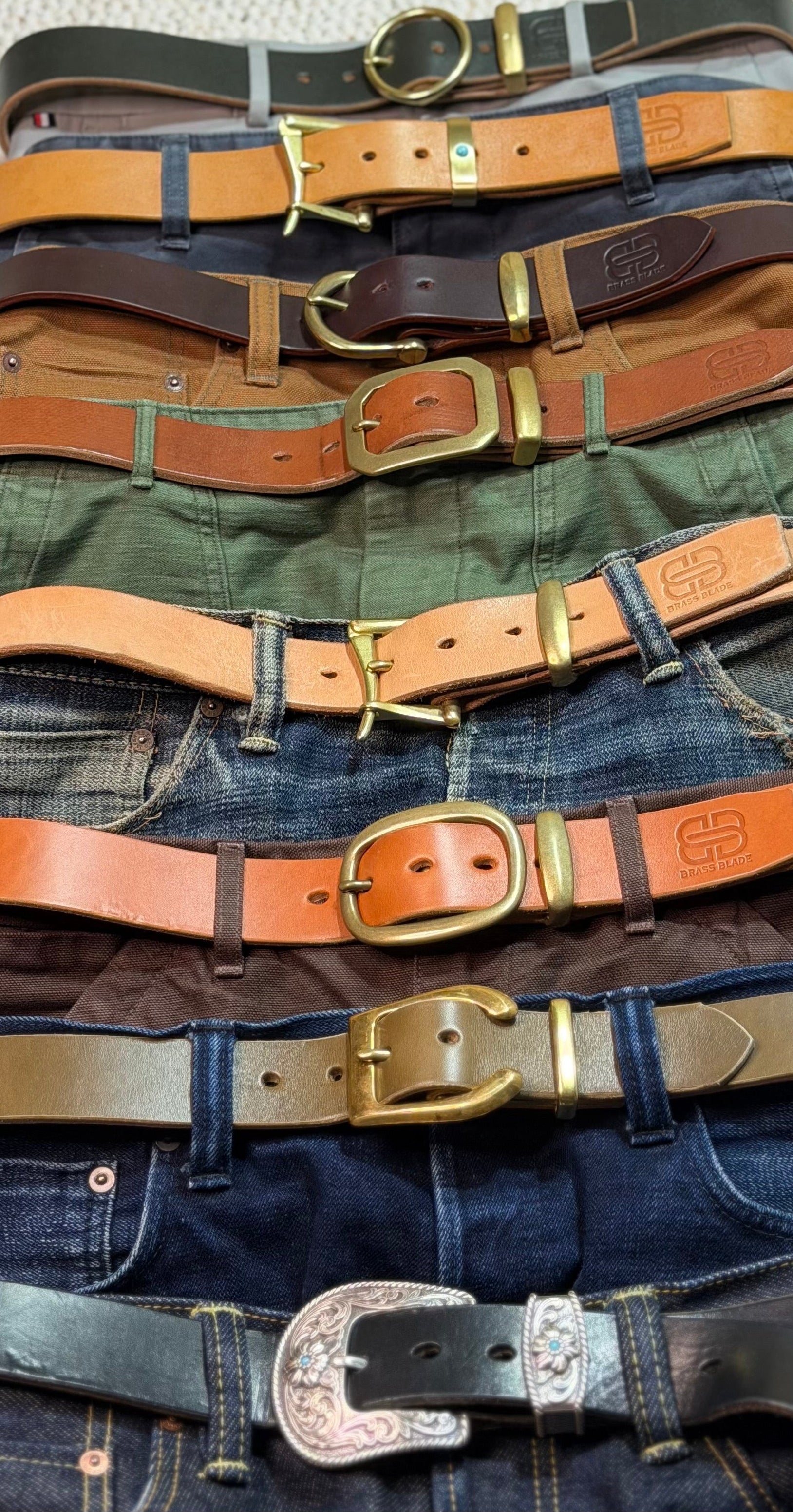 Eight pants and jeans with different leather belts arranged top to bottom