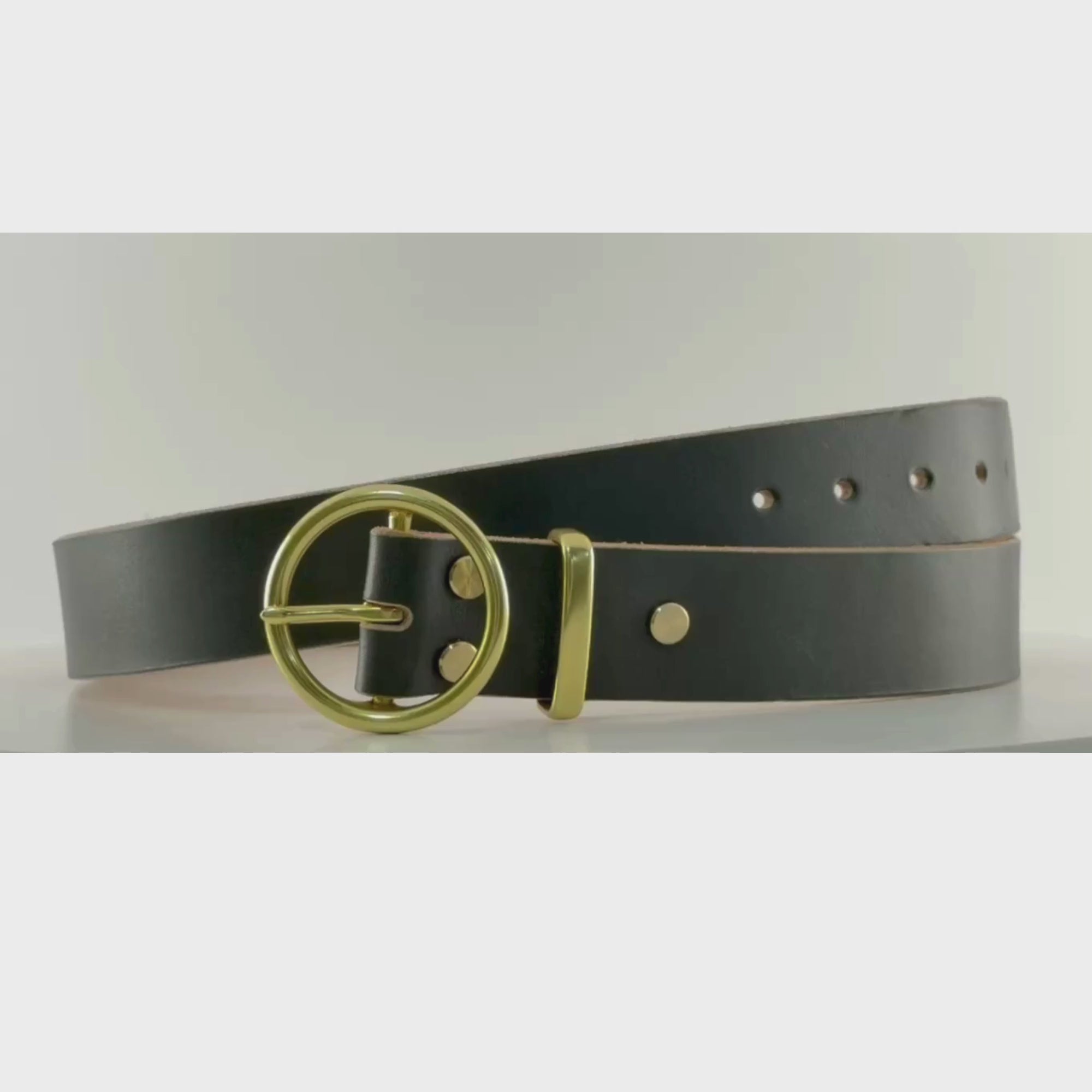 Video of a dark green leather belt with a circular brass buckle on a carousel