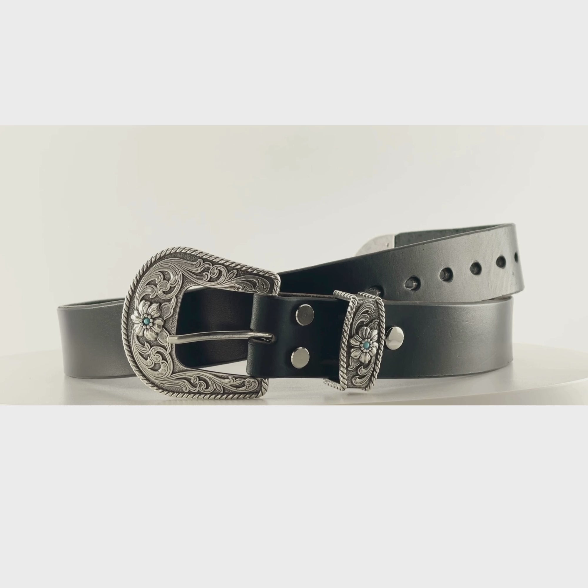 Video of a black leather belt with a silver engraved western buckle on a carousel