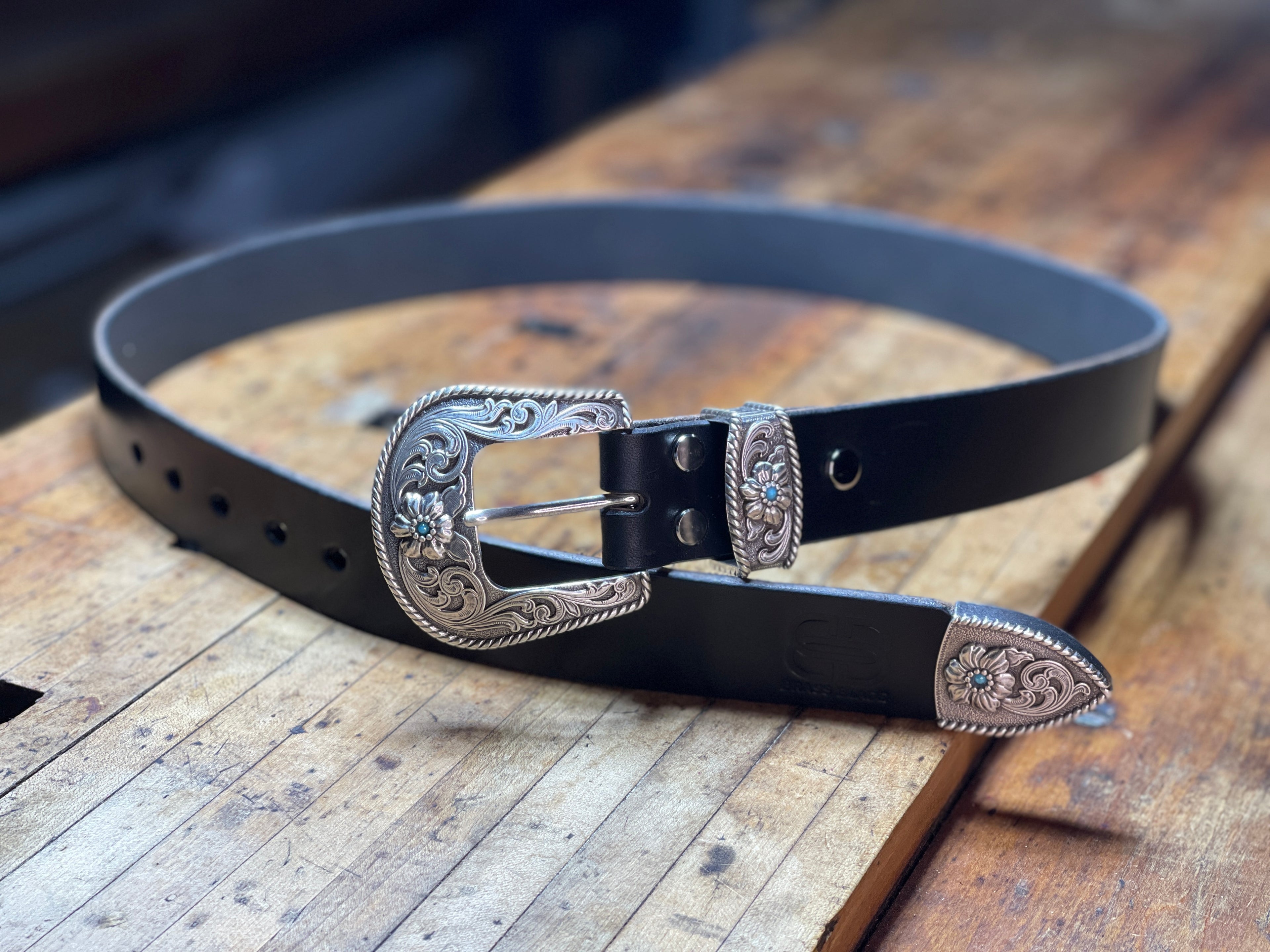 Black leather belt with silver buckle on a wooden surface