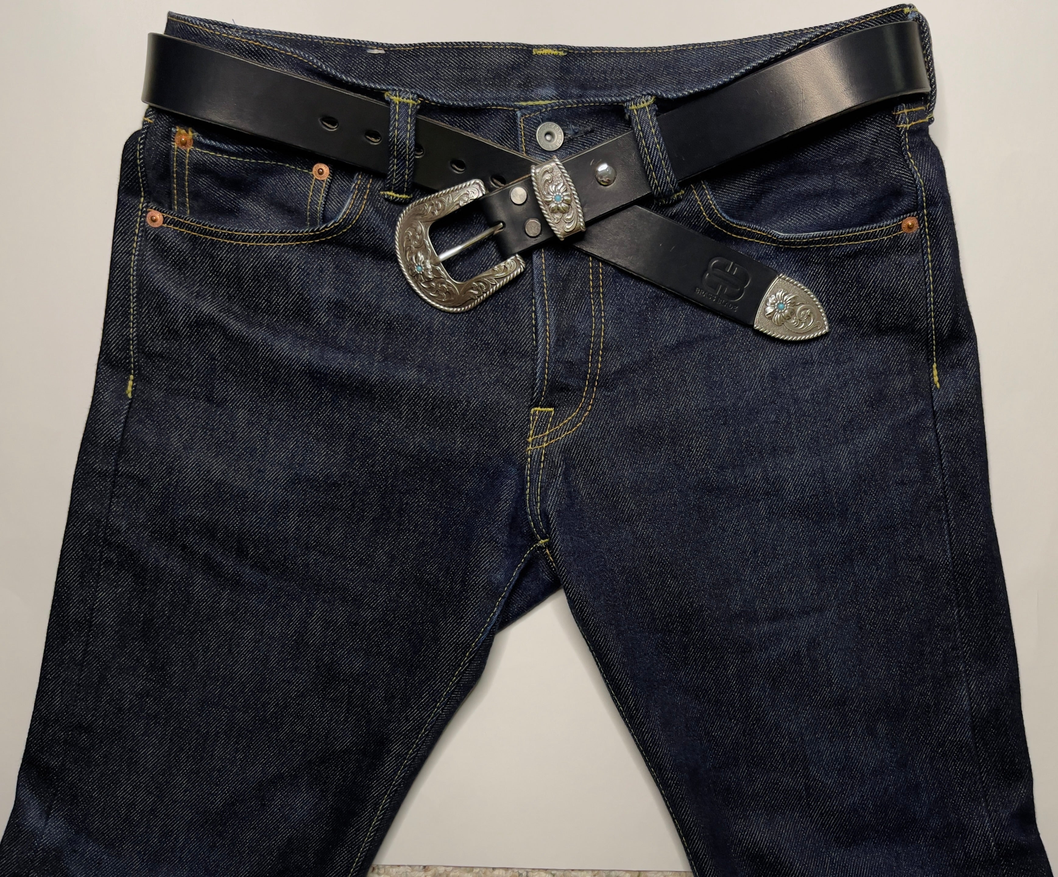 Dark blue jeans with a black belt and silver buckle on a light gray background
