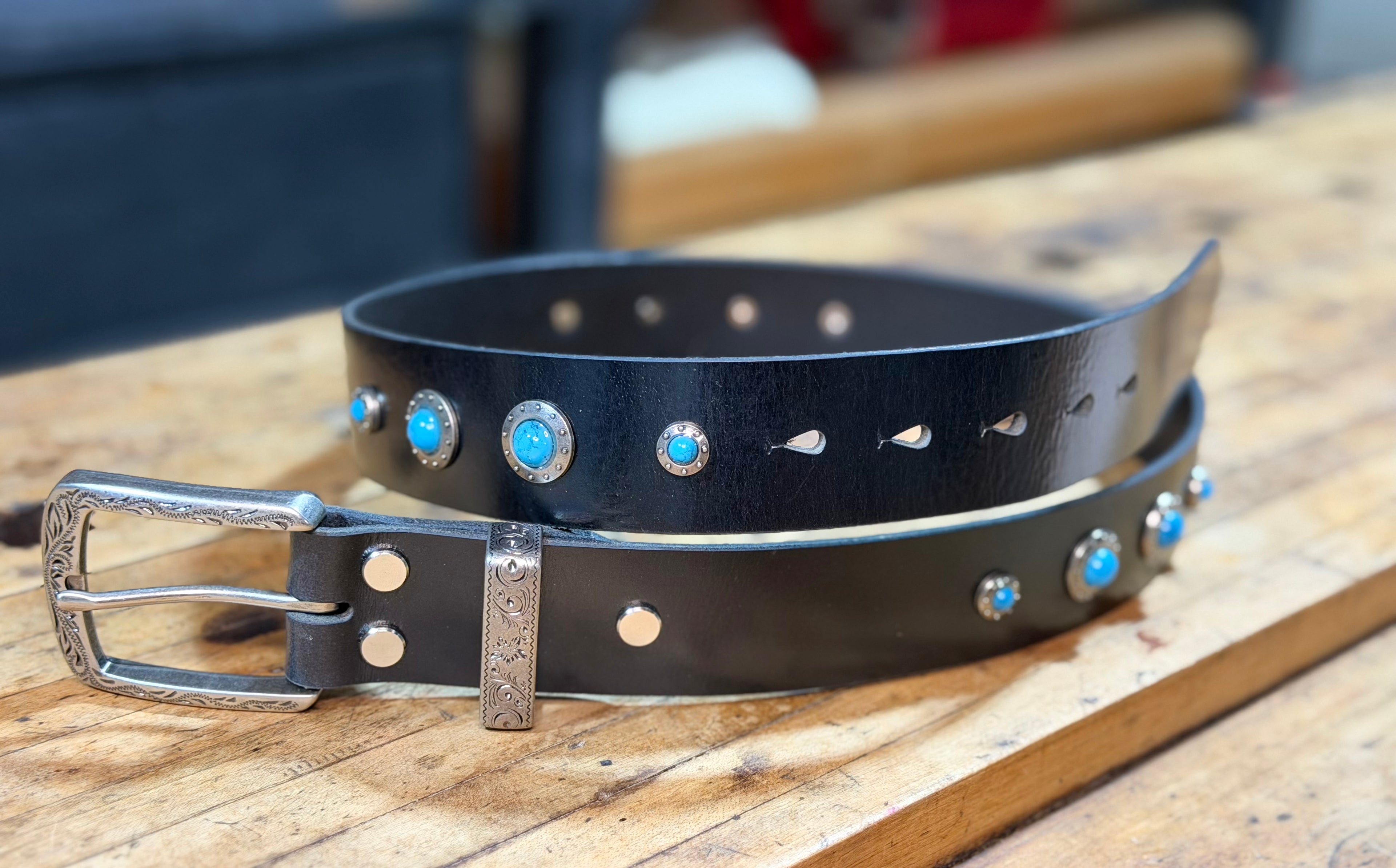 Black leather belt with silver buckle and turquoise conchos on a wooden surface