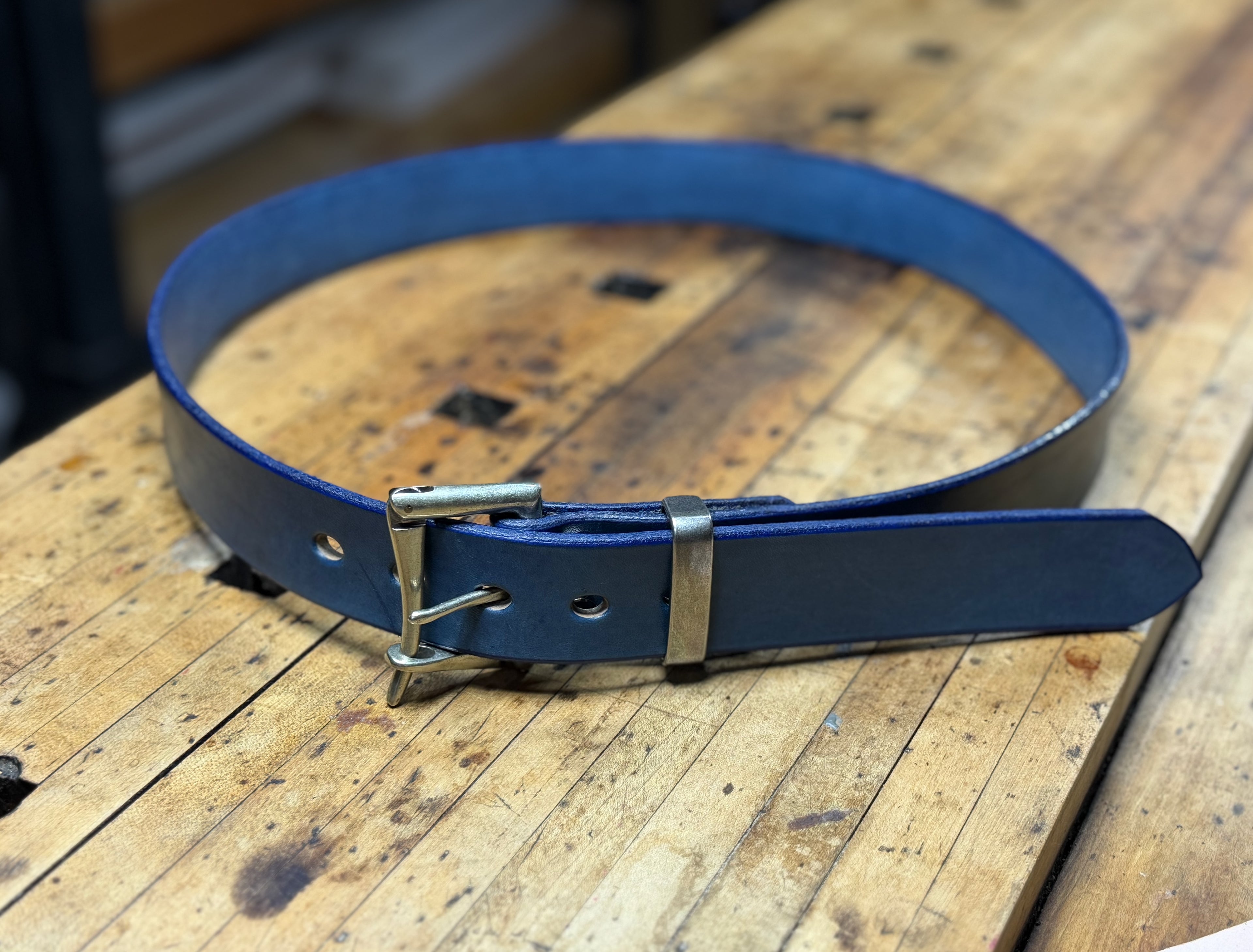 Blue leather belt with a silver buckle on a wooden workbench