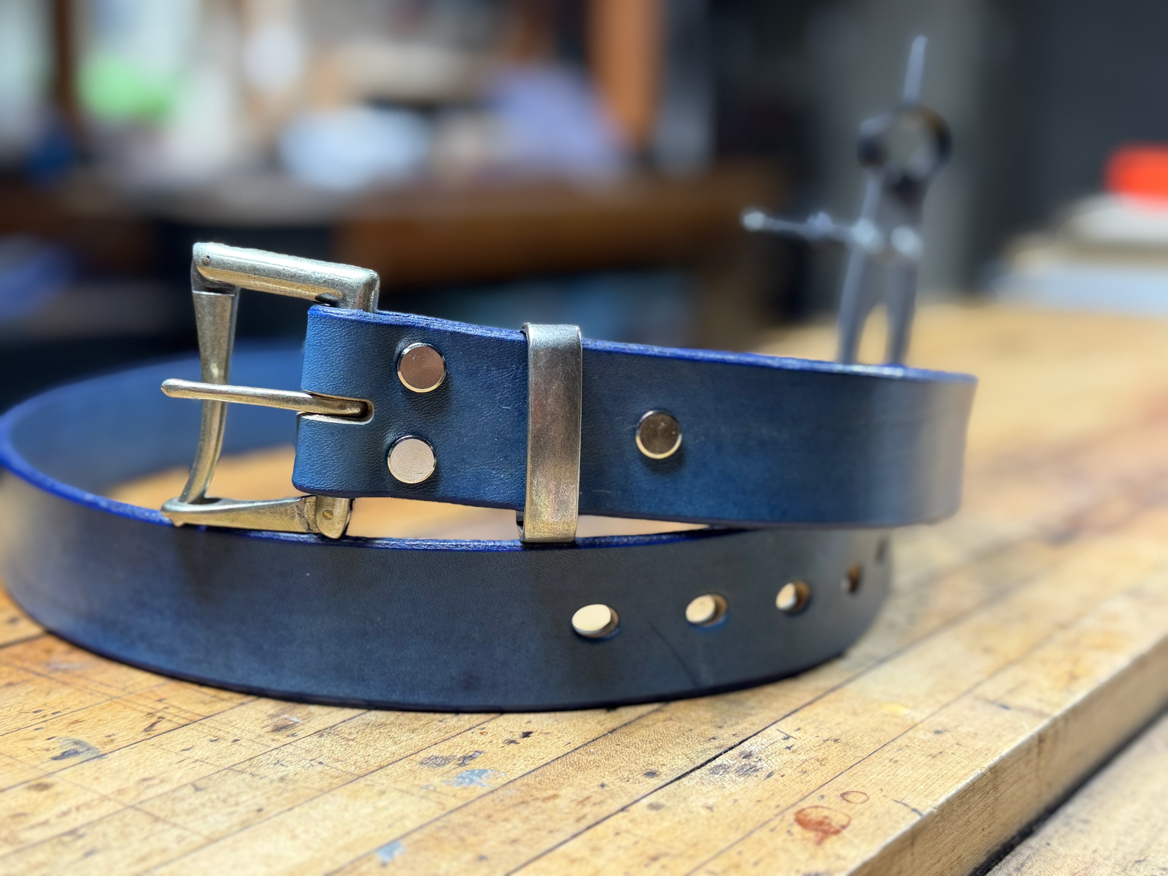 Blue leather belt with silver buckle on a wooden workbench