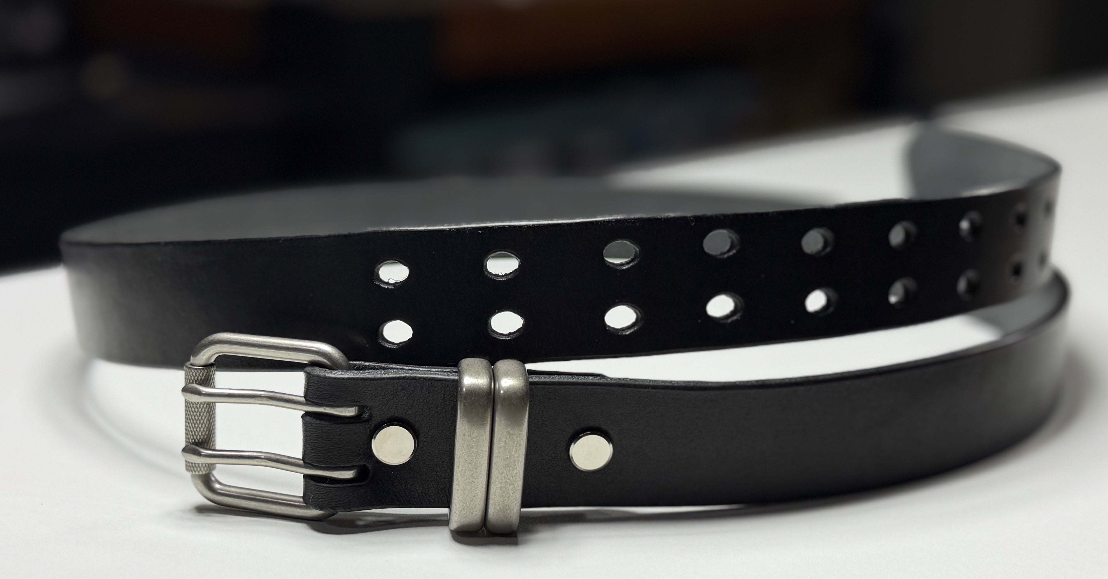 Black leather belt with silver buckle on a white surface
