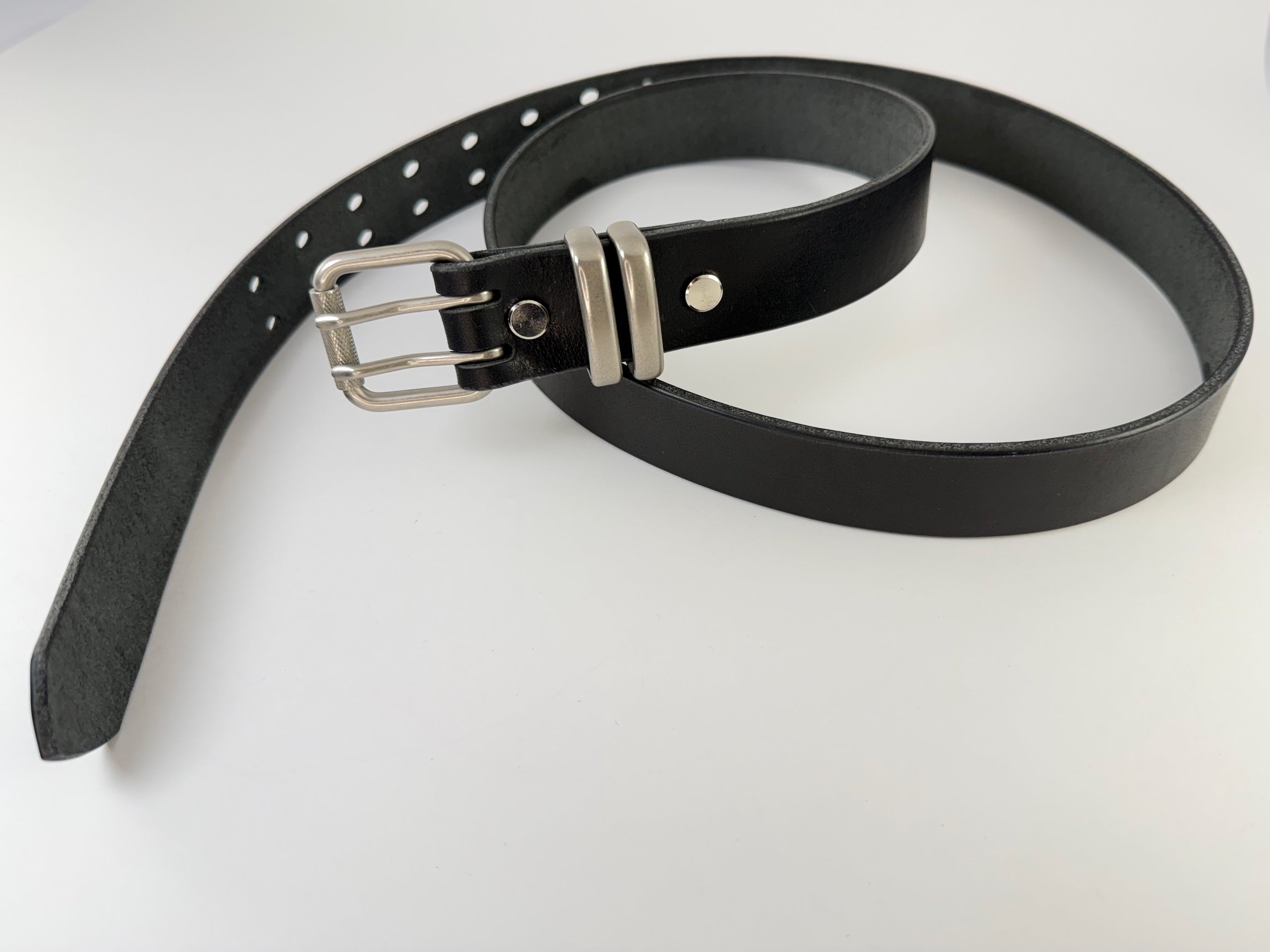 Black leather belt with silver buckle in a coiled position on a white background.