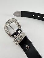 Black western cowboy belt with silver buckle and keeper adorned with turquoise stones on a light gray background