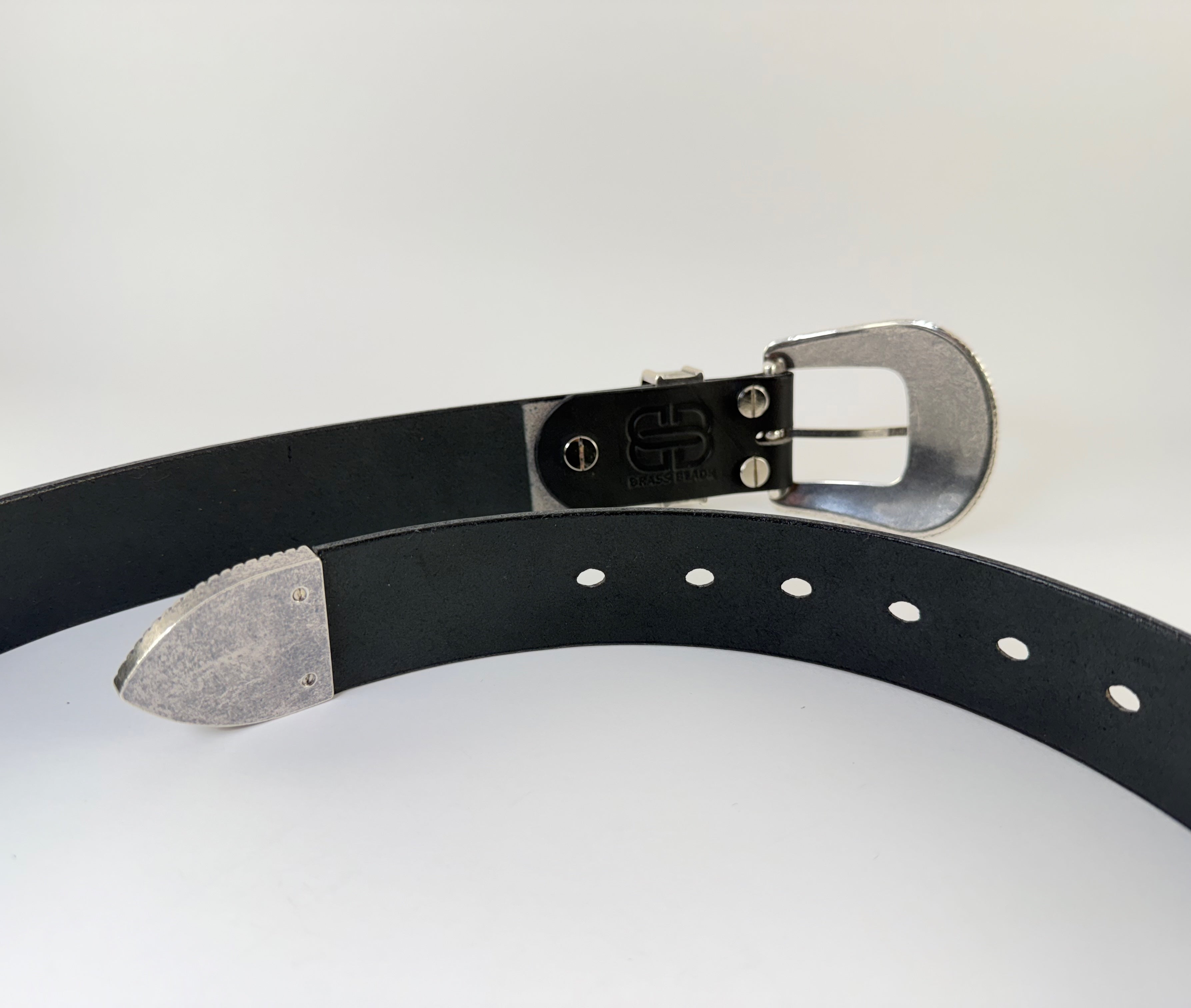 The back side of a black western cowboy belt with silver buckle and keeper on a light gray background