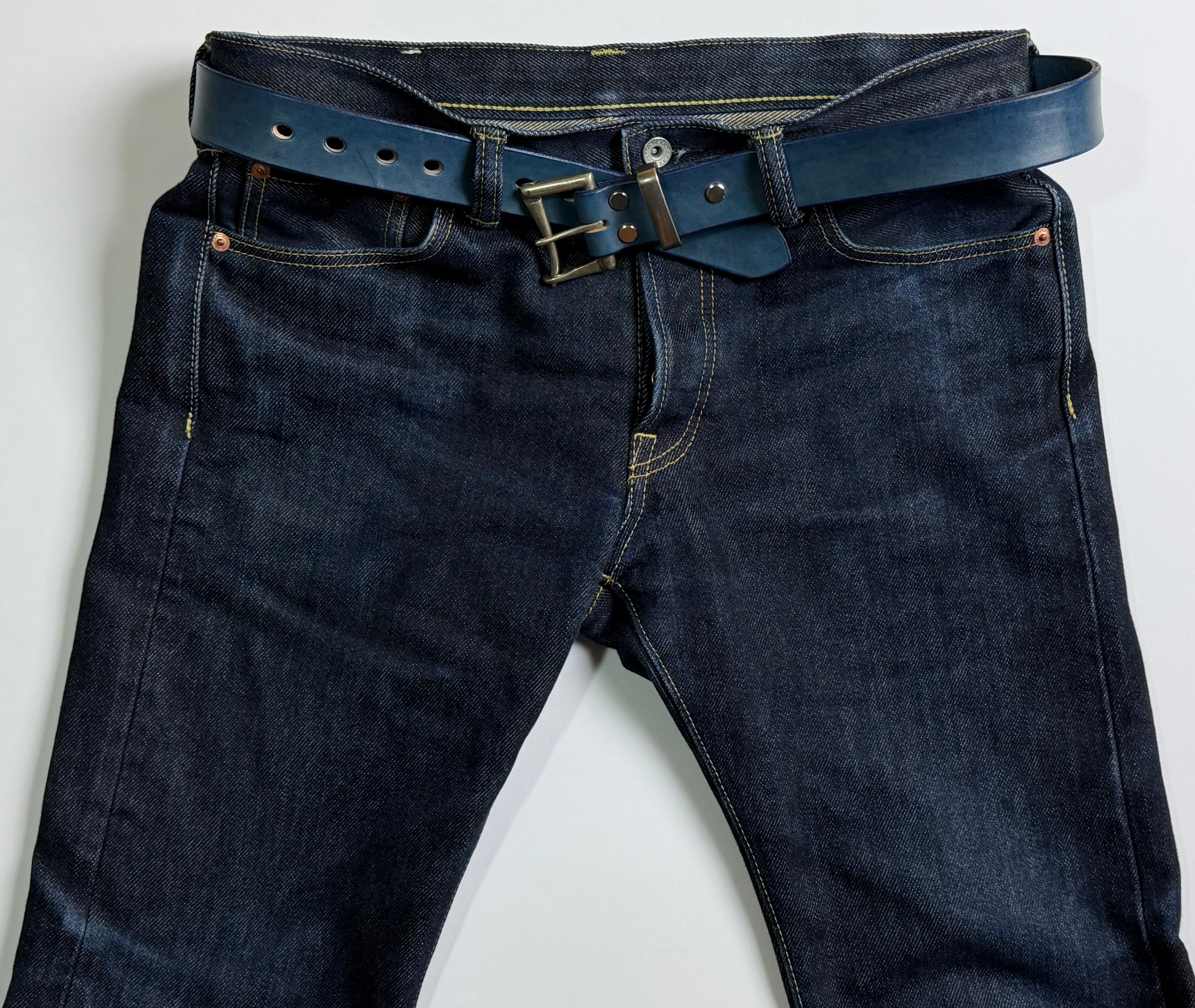 Dark blue jeans with a blue indigo-dyed belt on a light gray background