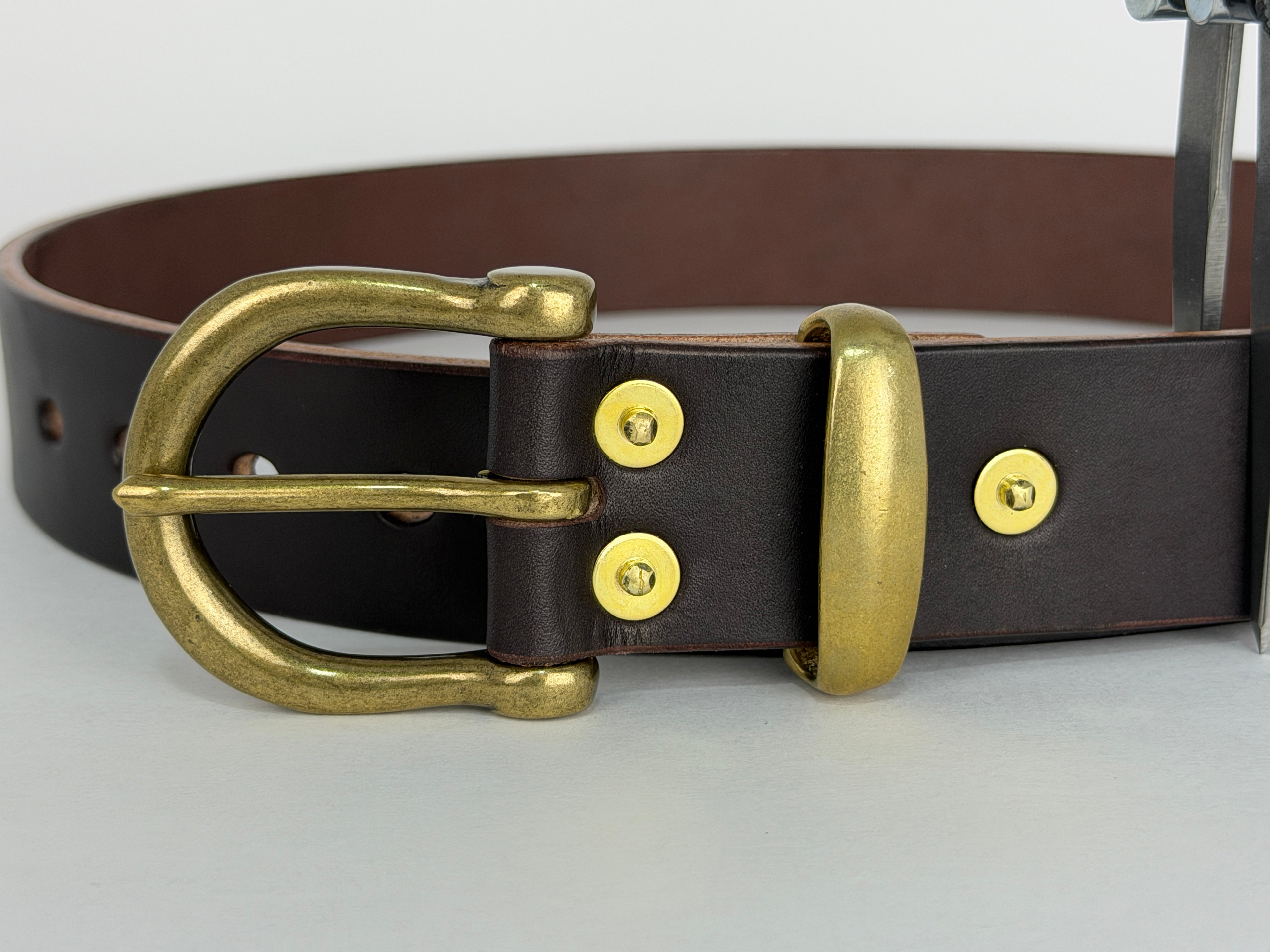 Close up picture of a brown leather belt with a brass buckle, keeper and rivets.