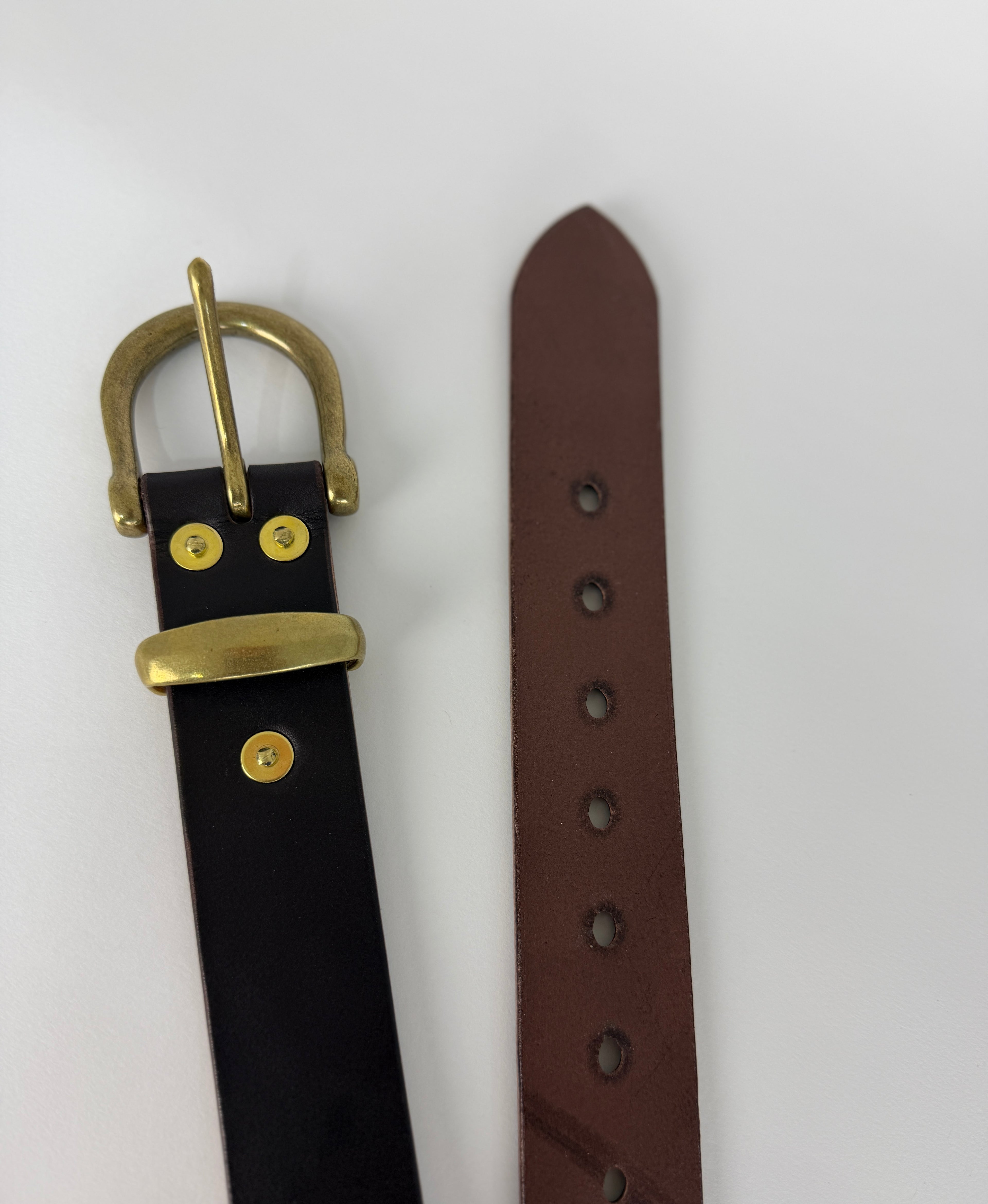 Top view picture of a brown leather belt showing a brass buckle, keeper, rivets as well as the edge of the belt.