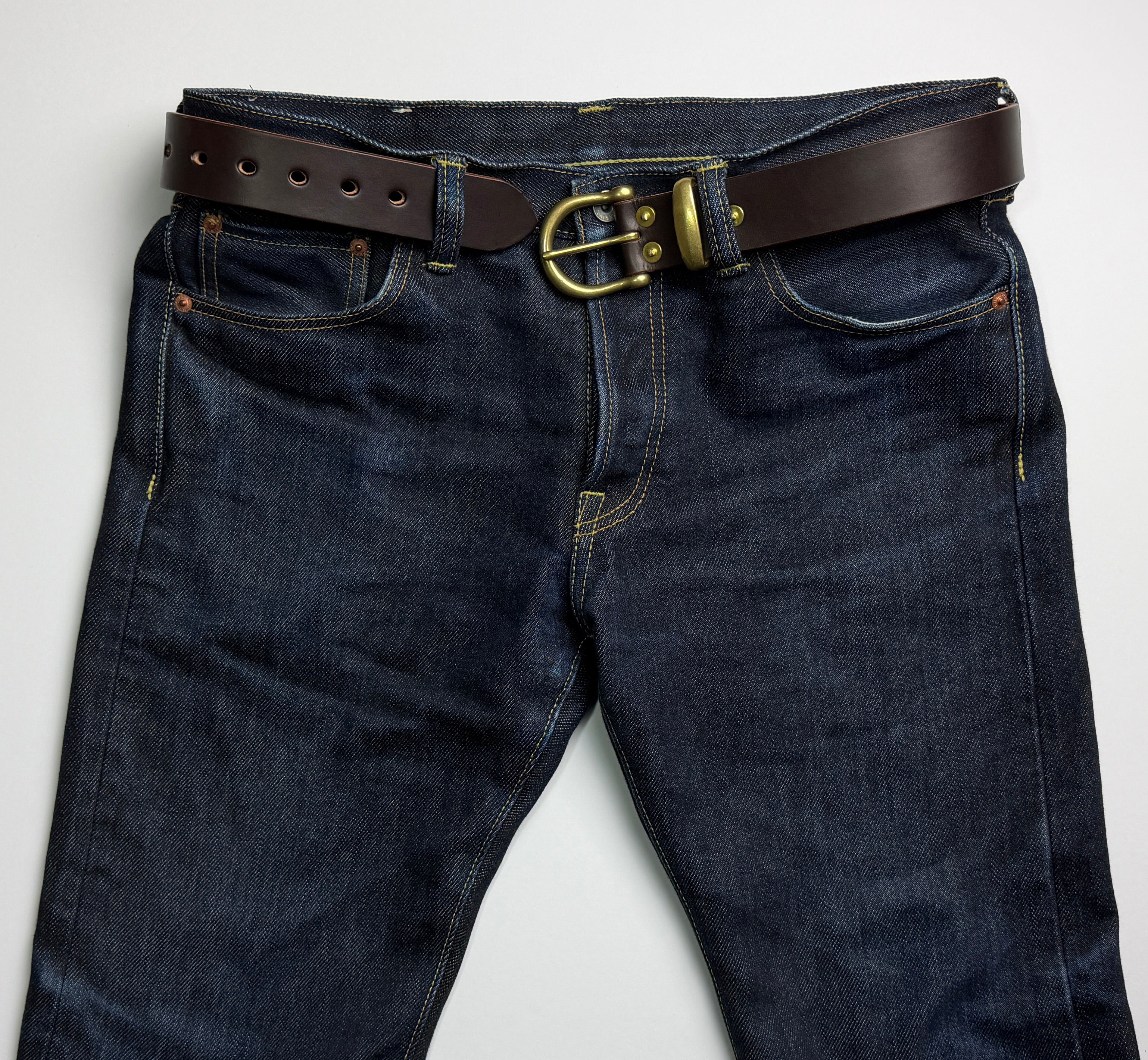 Picture of a brown leather belt with brass buckle and hardware worn on a pair of blue denim jeans.