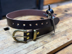 Brown leather belt with brass buckle, keeper and rivets on a wooden workbench
