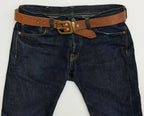 Brown leather belt with brass buckle, keeper and copper rivets on dark blue jeans.  The buckle of the belt is octagonal-shaped.