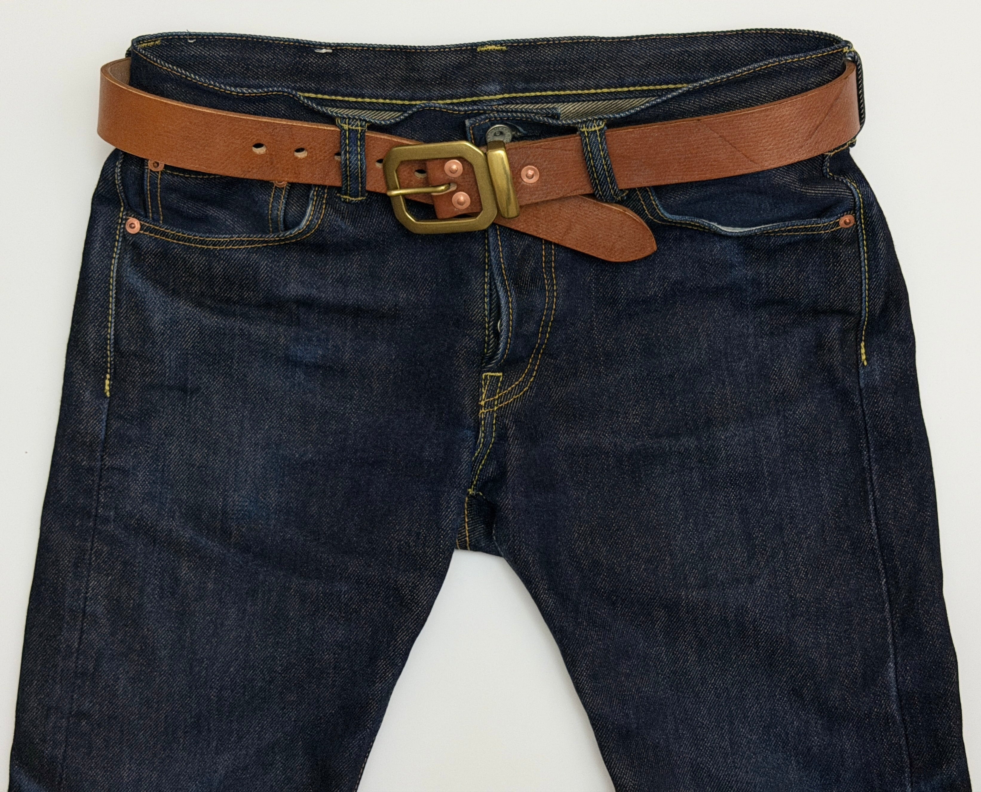Brown leather belt with brass buckle, keeper and copper rivets on dark blue jeans.  The buckle of the belt is octagonal-shaped.
