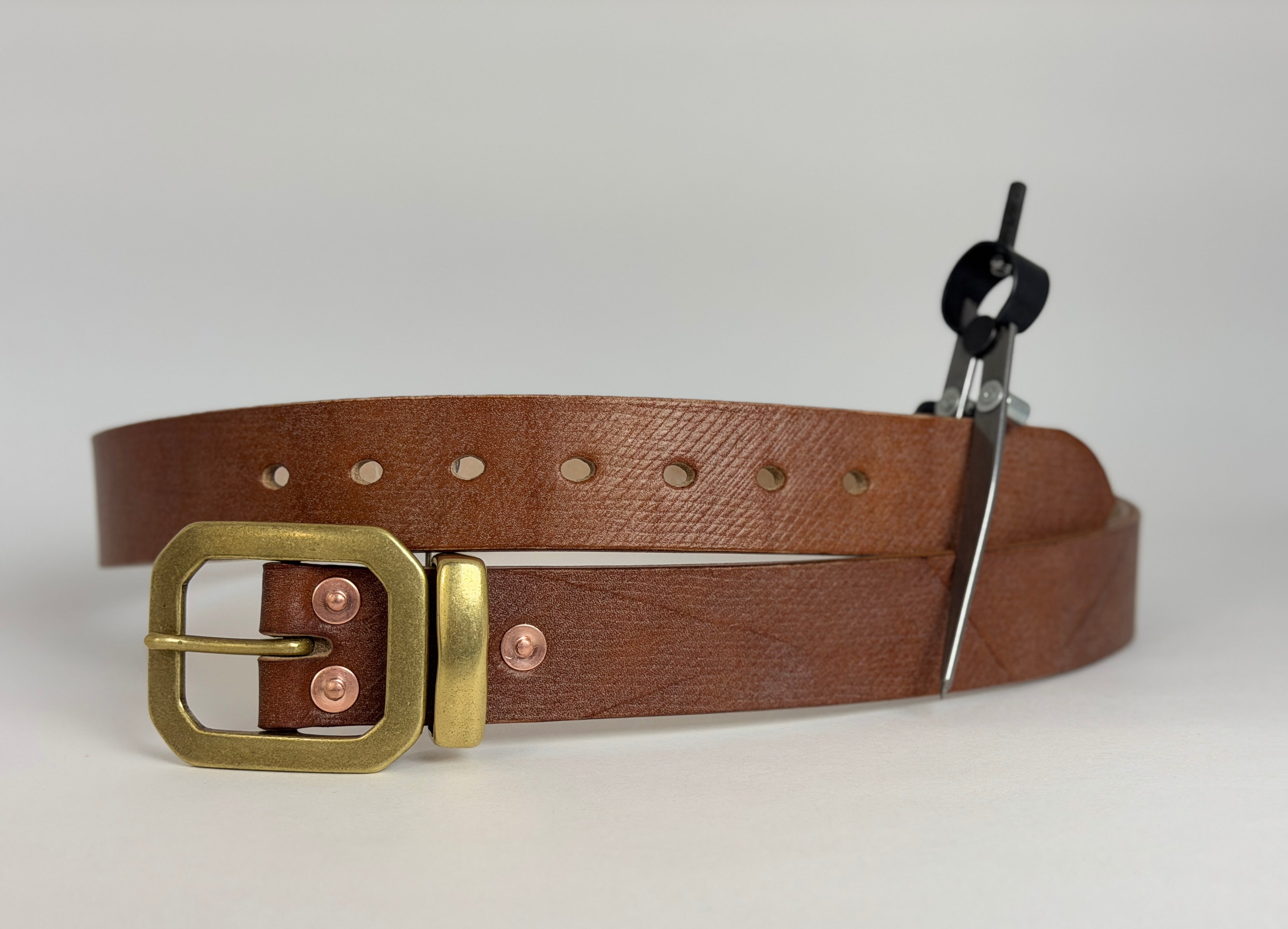 Brown leather belt with brass buckle, keeper and copper rivets on a white background