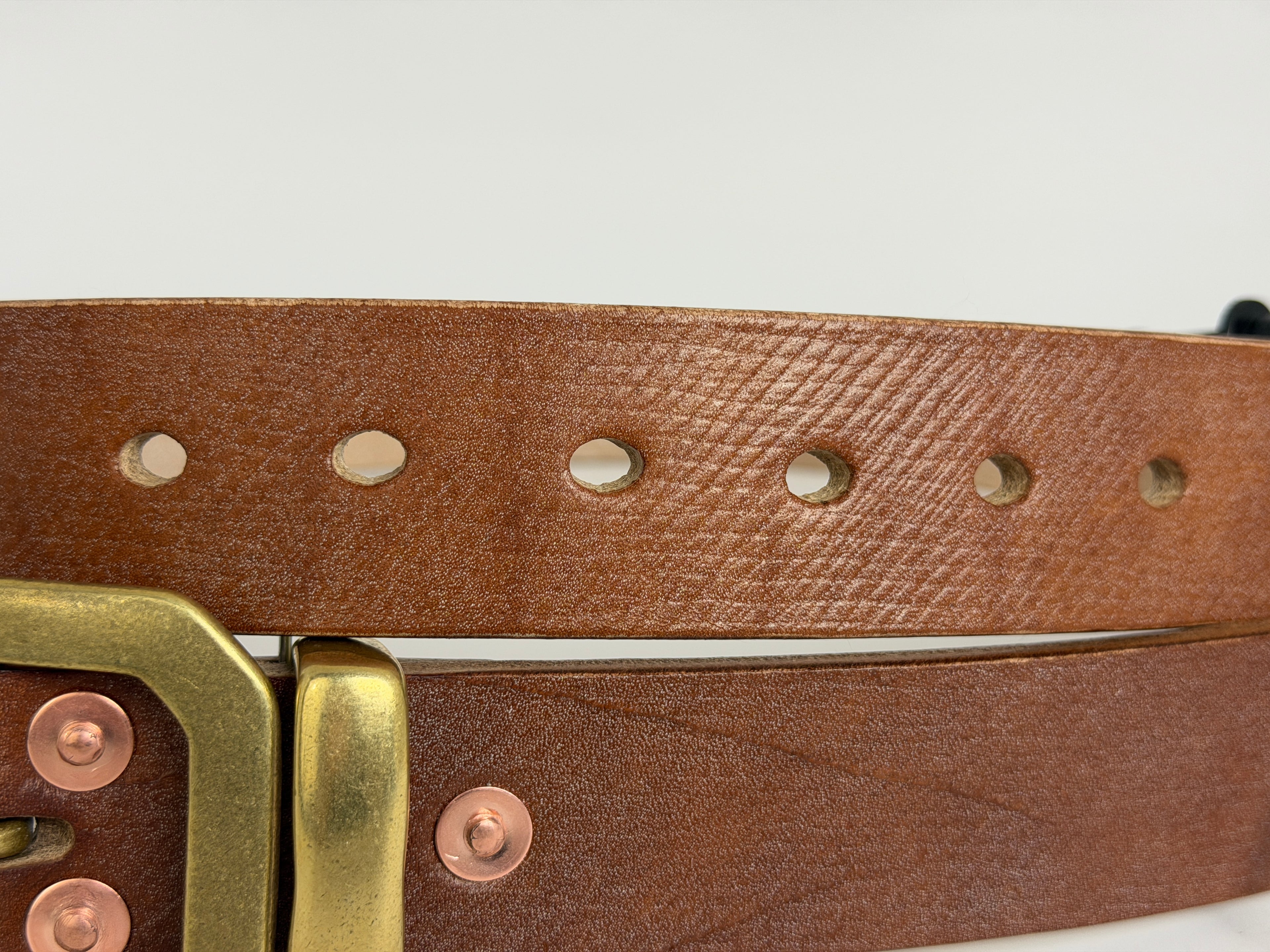 Closeup view of the cross hatch pattern on a brown leather belt highlighting the 7 punched holes on the belt.