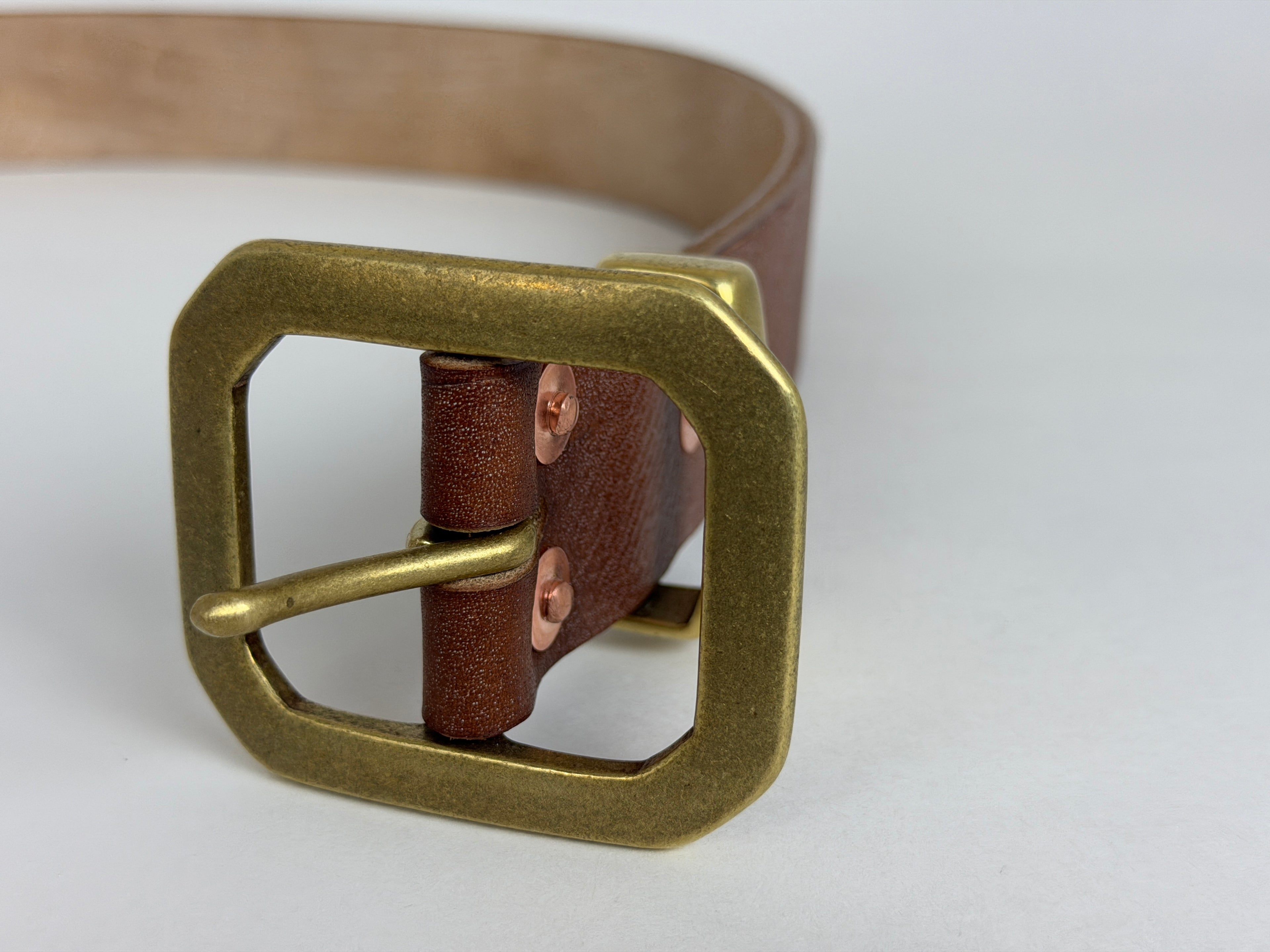 Closeup frontal view of an octagonal solid brass buckle on a brown leather belt on a white background.