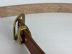 Closeup top view of a brass buckle, keeper and copper rivets on a white background.