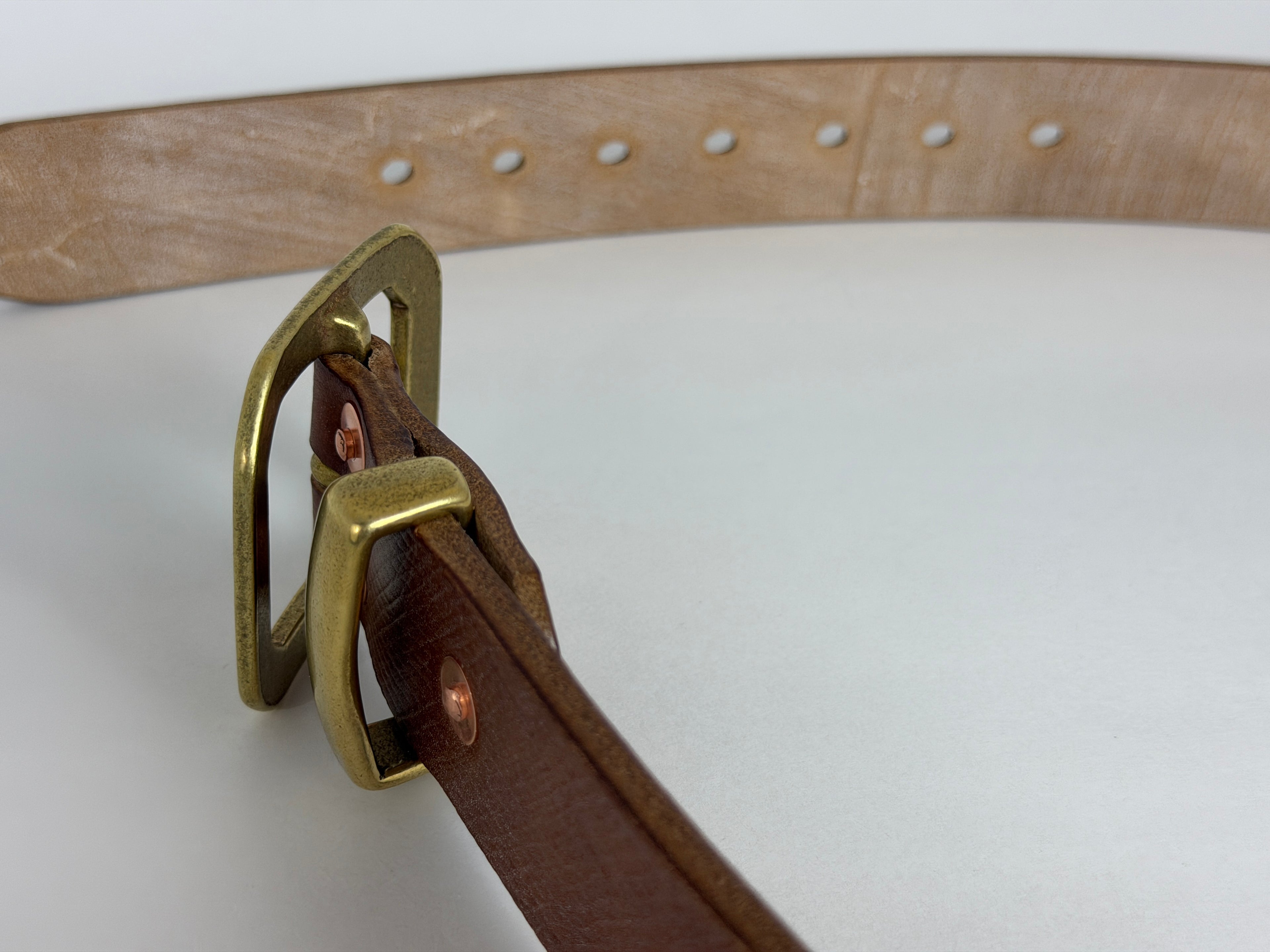 Closeup top view of a brass buckle, keeper and copper rivets on a white background.