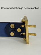 Close-up of the back of a navy blue leather belt with brass hardware on a light gray background.  The Chicago screws are being highlighted as an option to brass rivets.