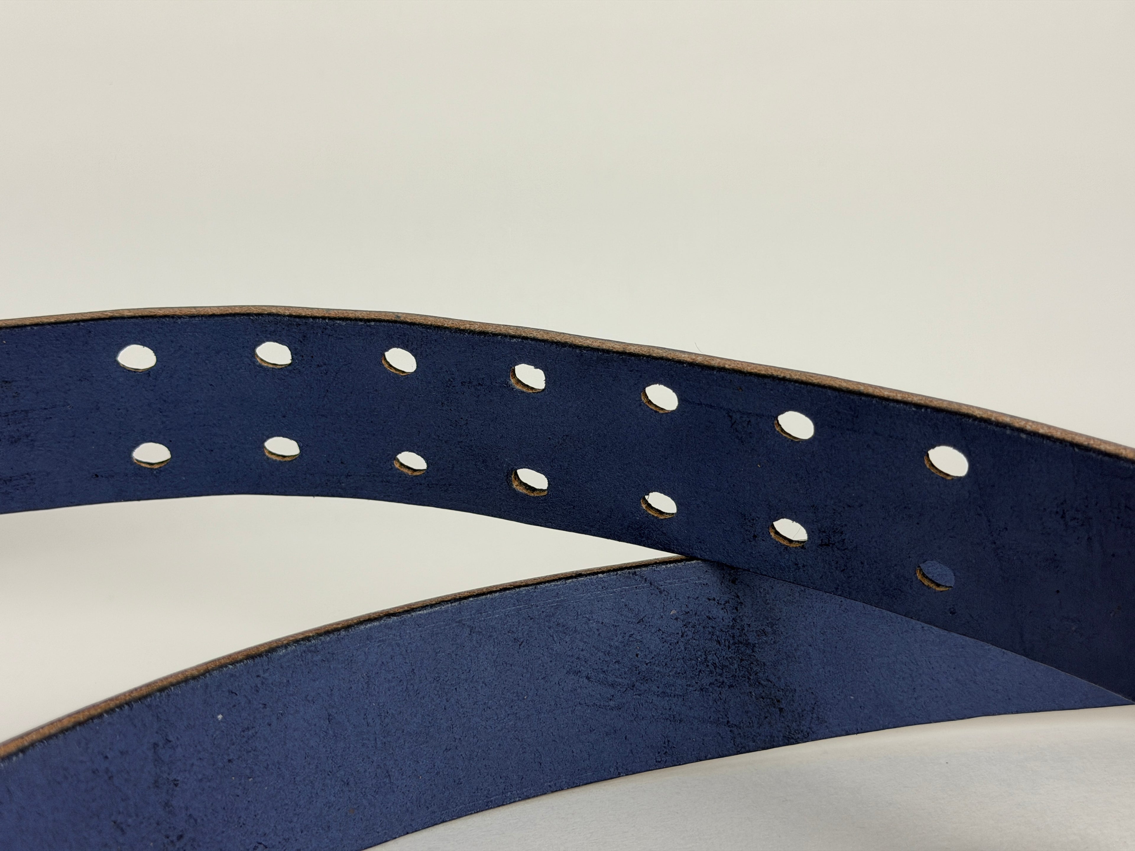Close-up of a Navy blue belt showing double-pronged belt holes on a white background 