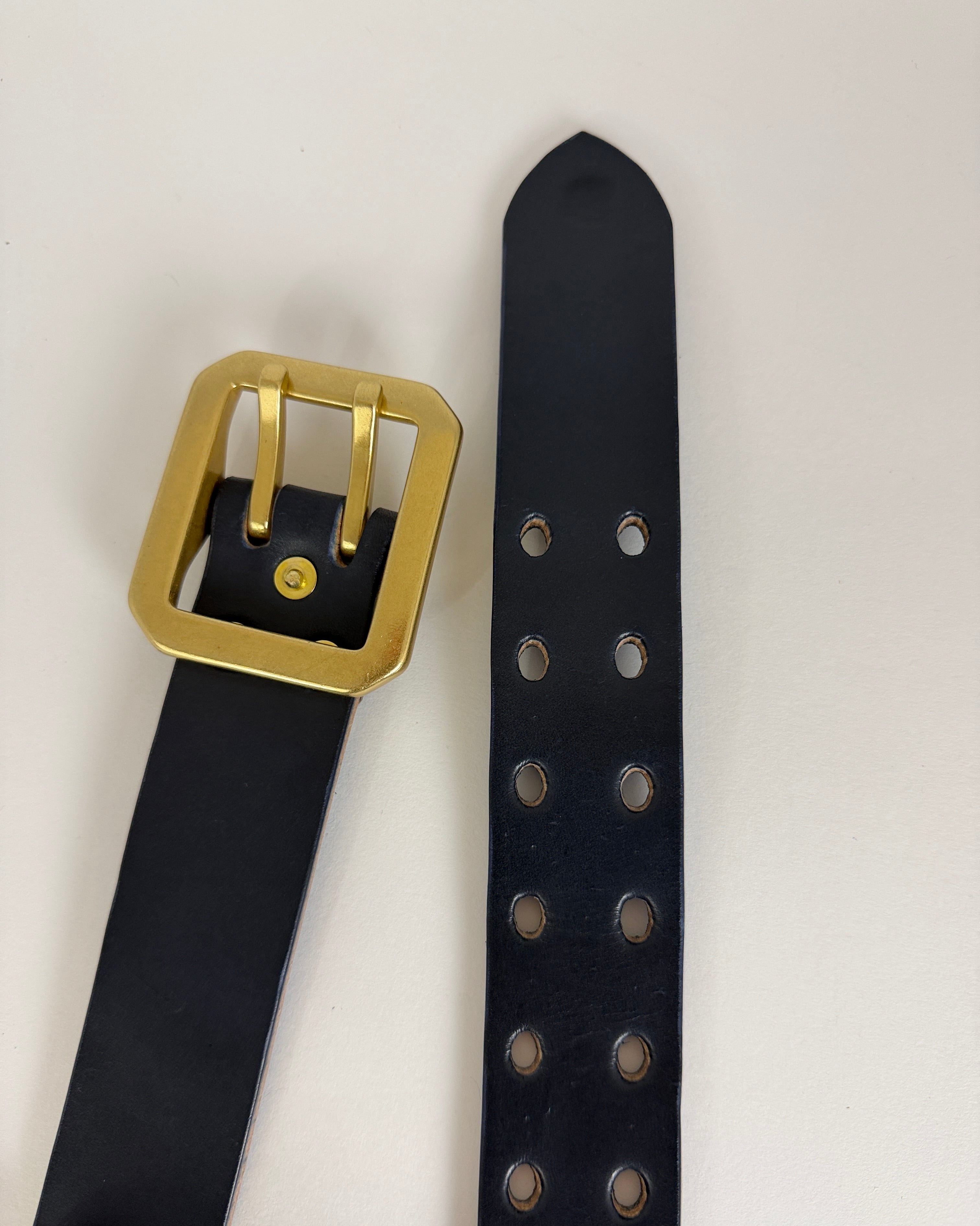 Top view of a Navy blue leather belt with a brass buckle on a light gray background 