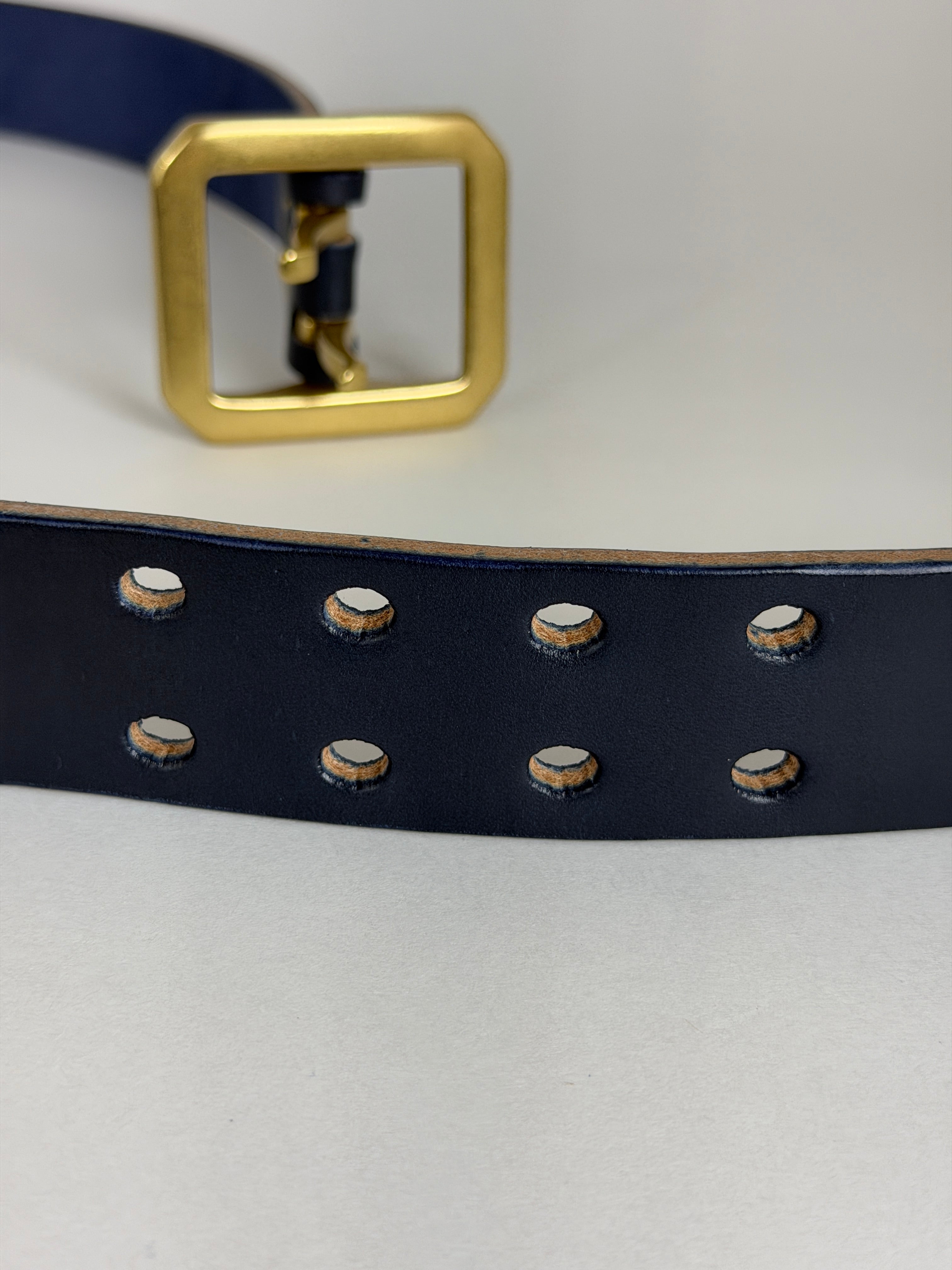 Navy blue leather belt with brass buckle on a light gray background
