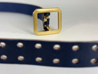Closeup of a navy blue leather belt with two pronged belt holes on a light gray background