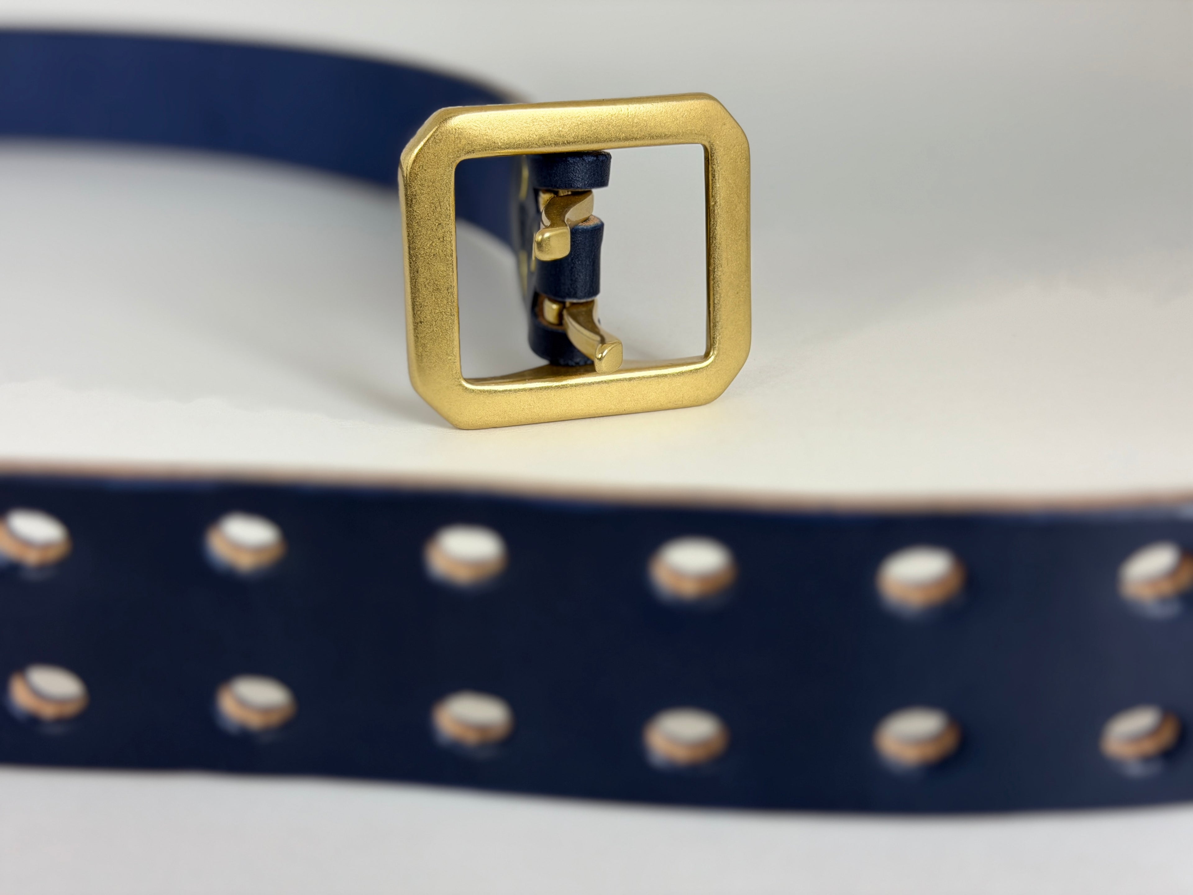 Closeup of a navy blue leather belt with two pronged belt holes on a light gray background