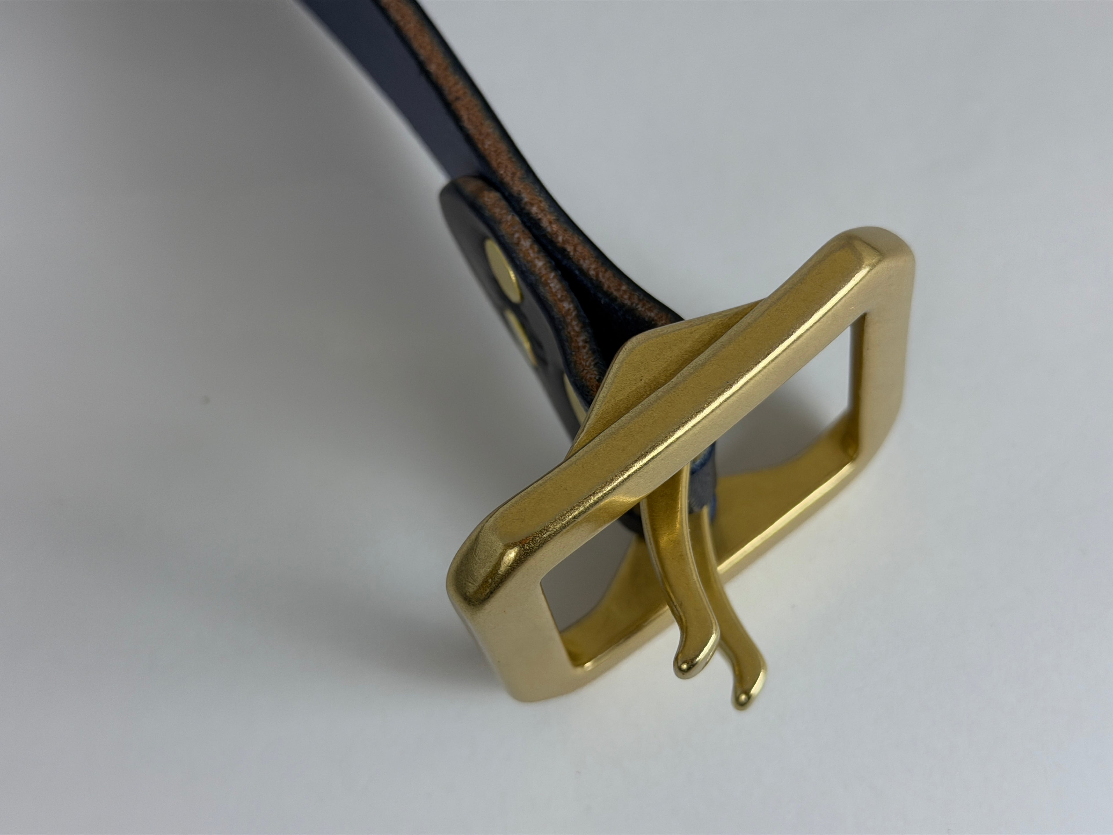 Top closeup view of a brass belt buckle on a white background