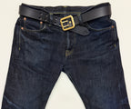 Dark blue jeans with a navy leather belt and brass buckle on a light background