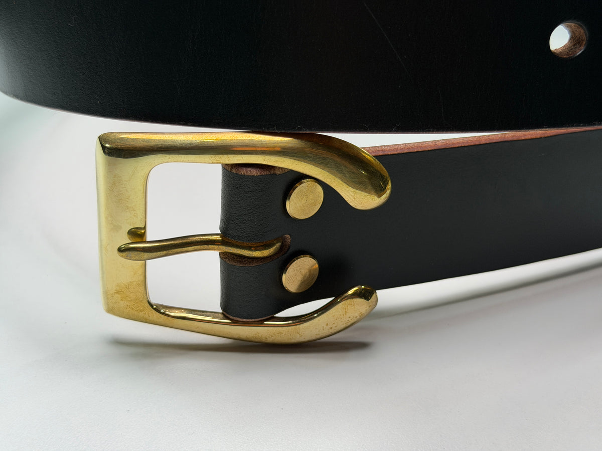 A close-up of a dark green belt on a white background.  This belt is made from dark green leather, with a brass horseshoe buckle and brass Chicago screws.
