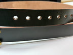Close-up of a dark green leather belt with brass-toned metal rivets and a tan interior lining, shown on a white surface.  This picture highlights the seven neatly punched oval belt holes.
