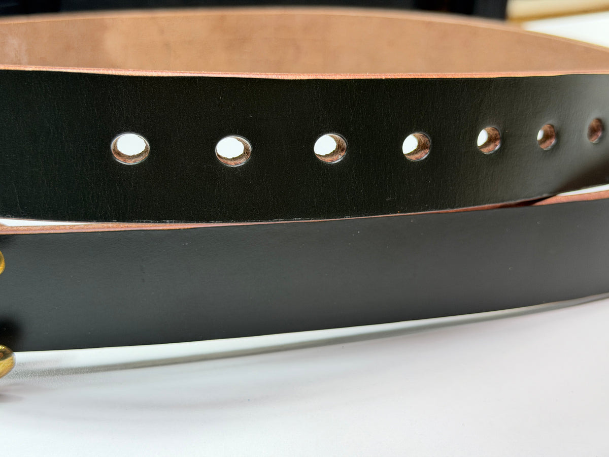 Close-up of a dark green leather belt with brass-toned metal rivets and a tan interior lining, shown on a white surface.  This picture highlights the seven neatly punched oval belt holes.