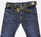 Dark green leather belt with a brass horseshoe  buckle, styled crossed over the waist of dark blue denim jeans on a white background.