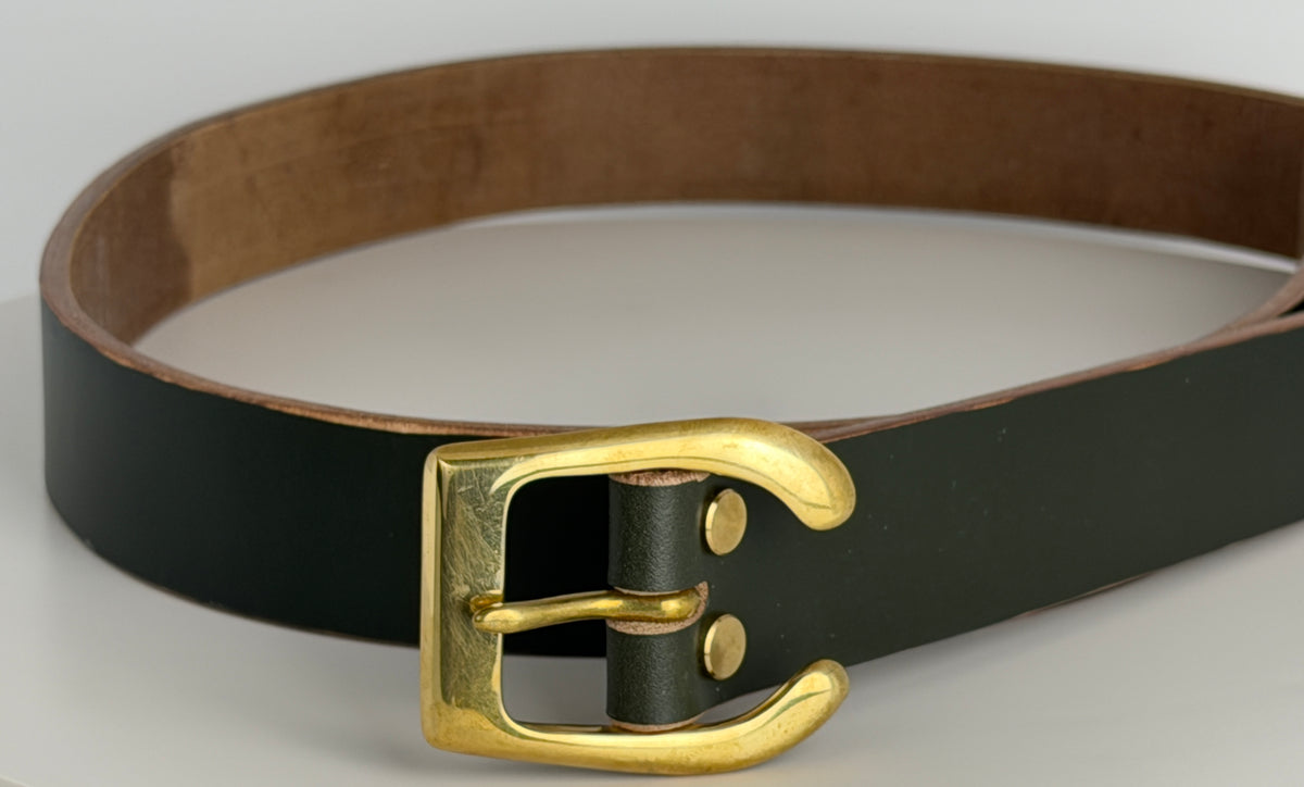 A close-up of a dark green belt on a white background.  This belt is made from dark green leather, with a brass horseshoe buckle and brass Chicago screws.