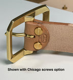 Close-up of a natural leather belt with a solid brass buckle attached with two brass Chicago screws on a white workbench.  There is a caption with the words 'Shown with Chicago screws option' at the bottom of the picture.