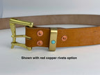 A tan leather belt with a brass buckle and keeper, shown on a white background with text reading 'Shown with red copper rivets option'. The belt has red copper rivets and a small turquoise accent on the keeper.