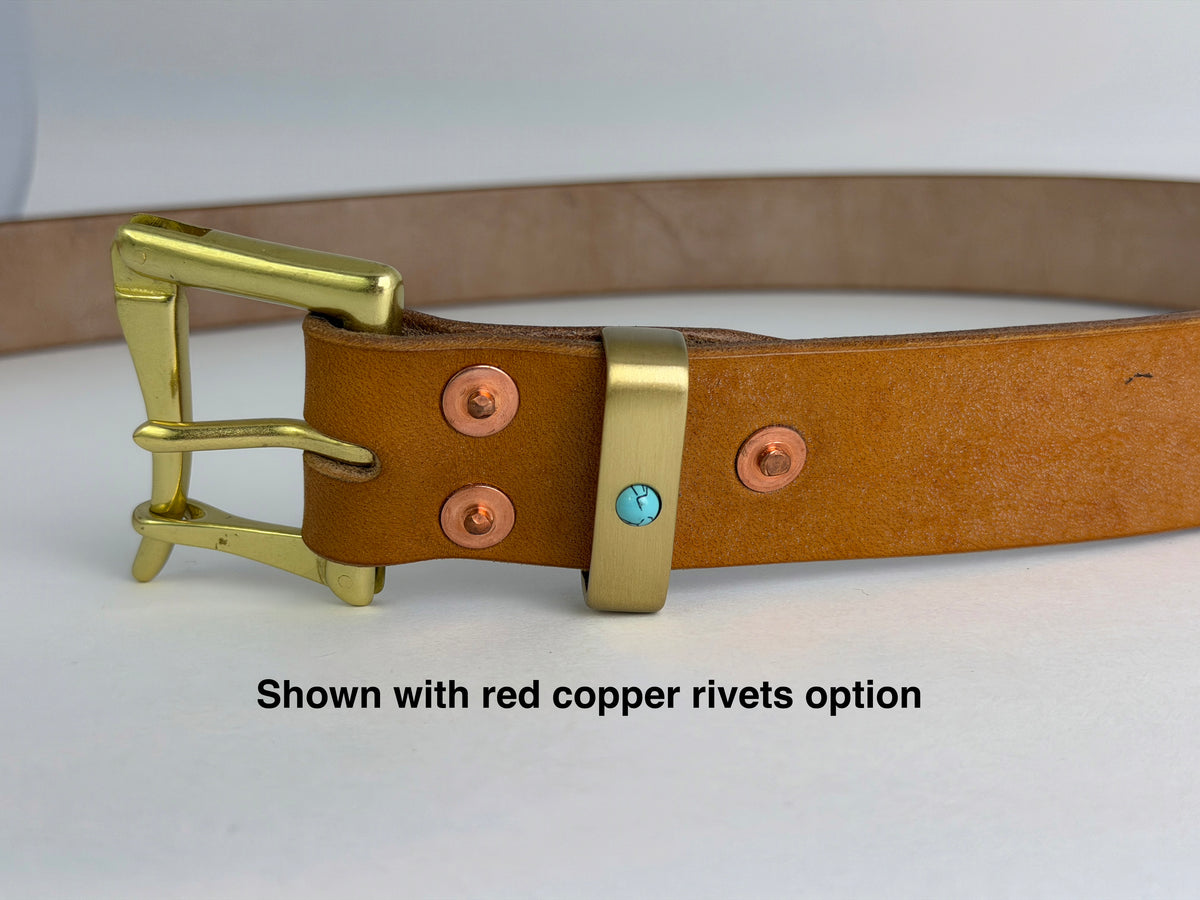 A tan leather belt with a brass buckle and keeper, shown on a white background with text reading 'Shown with red copper rivets option'. The belt has red copper rivets and a small turquoise accent on the keeper.