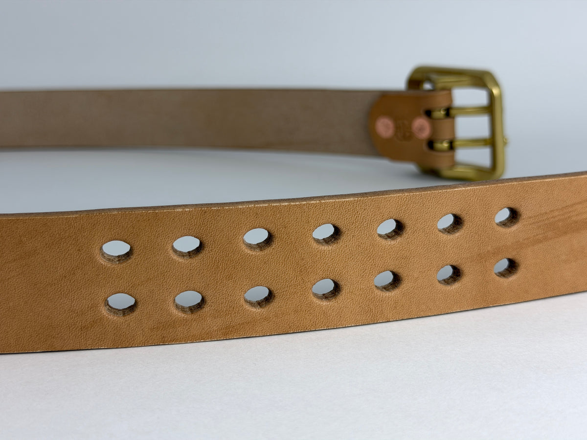 A close-up of a natural leather belt with a double row of oval cutouts and a brass buckle, shown against a light gray background.