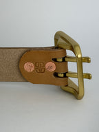 A close-up of the back of a natural leather belt with a heavy polished rectangular brass buckle.  The buckle is attached using solid copper rivets and shows a small "BB" logo that is embossed on the leather.
