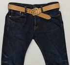 Dark blue denim jeans with a natural leather belt and dual-pronged brass buckle, laid flat against a light gray background.