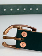 Close-up of a dark green leather belt with a copper horseshoe metal buckle and copper rivets, shown on a light gray background.
