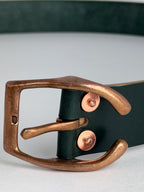 A close-up of a dark green leather belt featuring a large copper horseshoe buckle and matching copper rivets, set against a neutral light gray background.