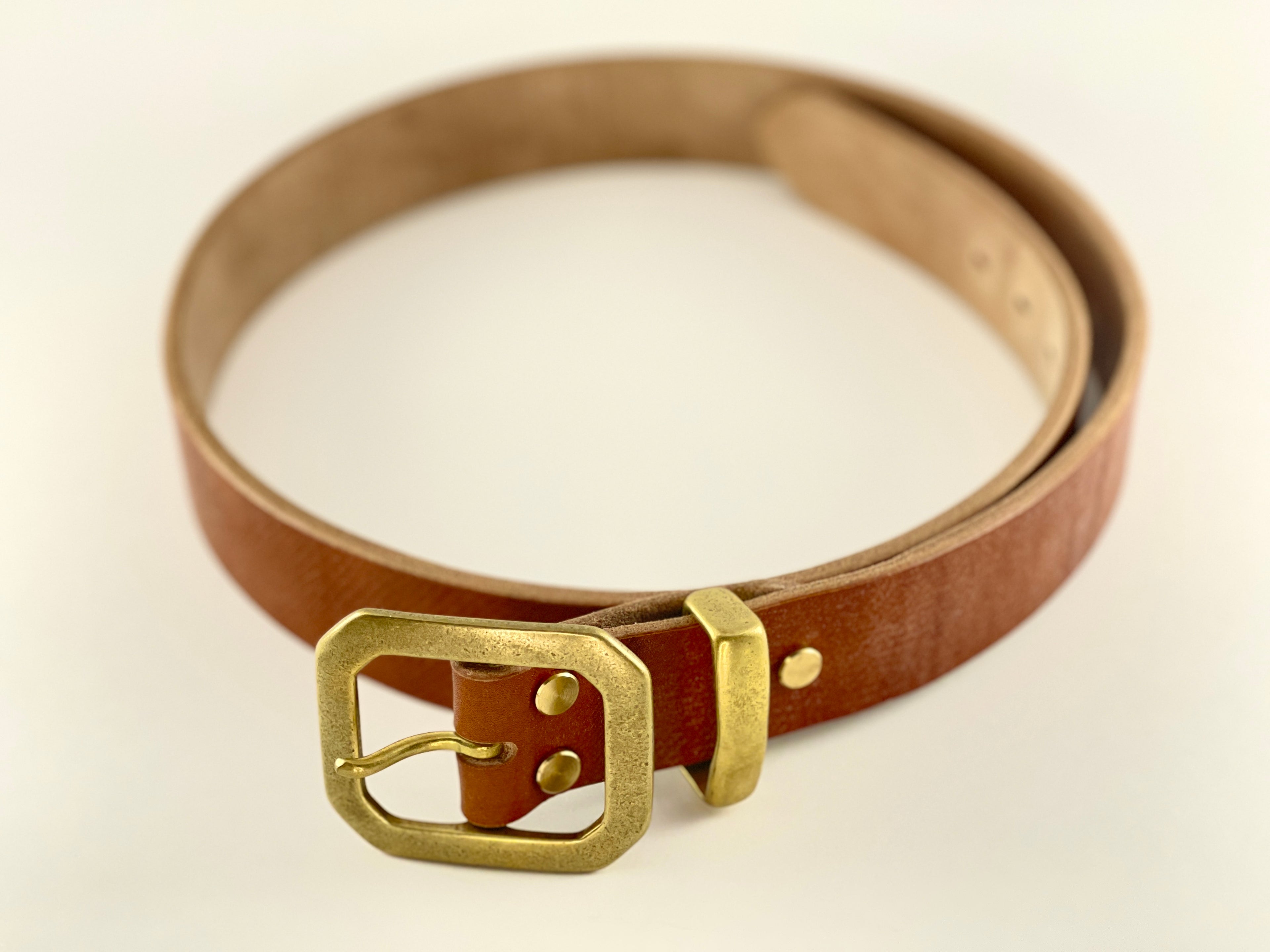 Brown leather belt with a brass buckle on a light beige background