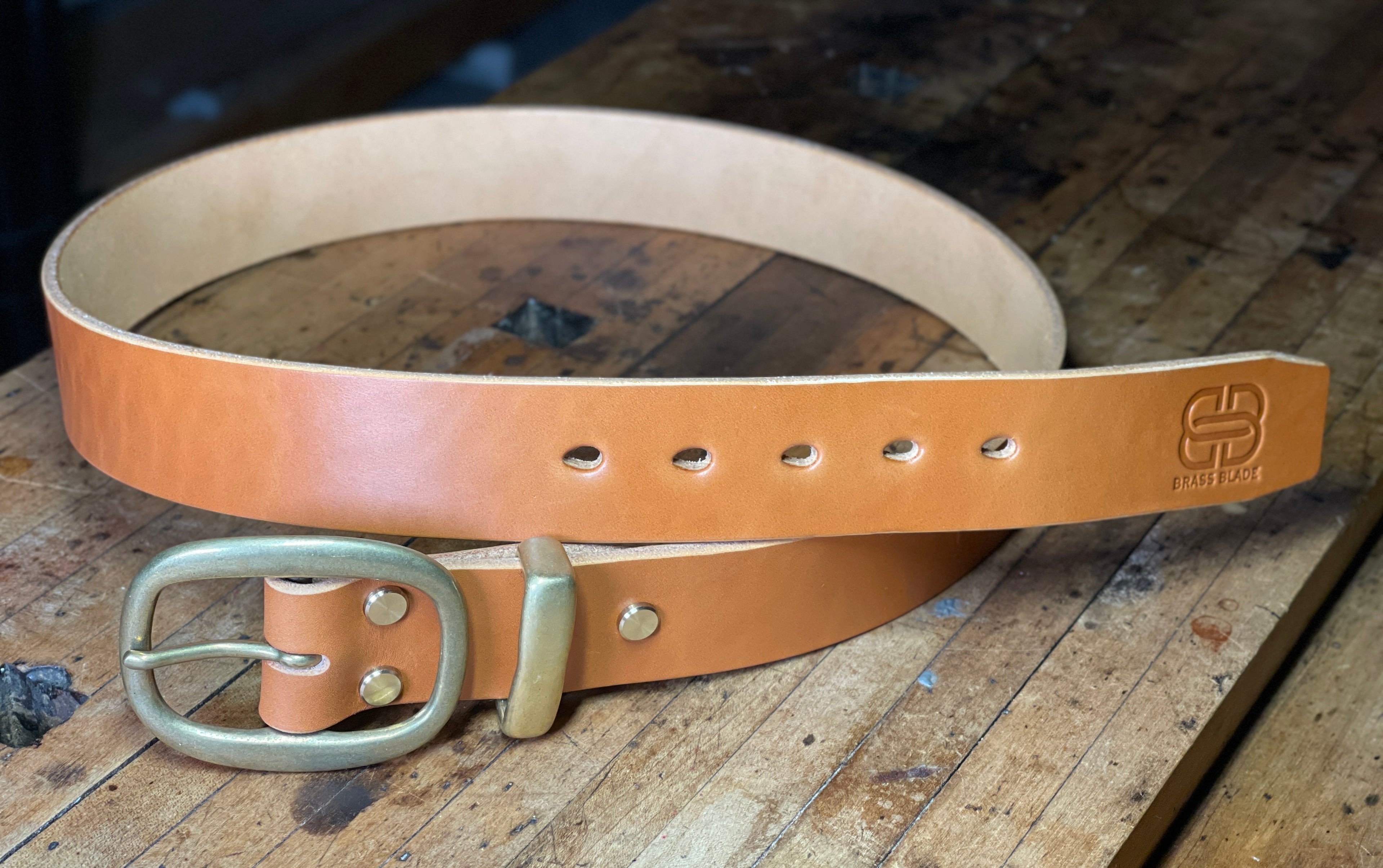 Brown leather belt with brass buckle on a wooden surface