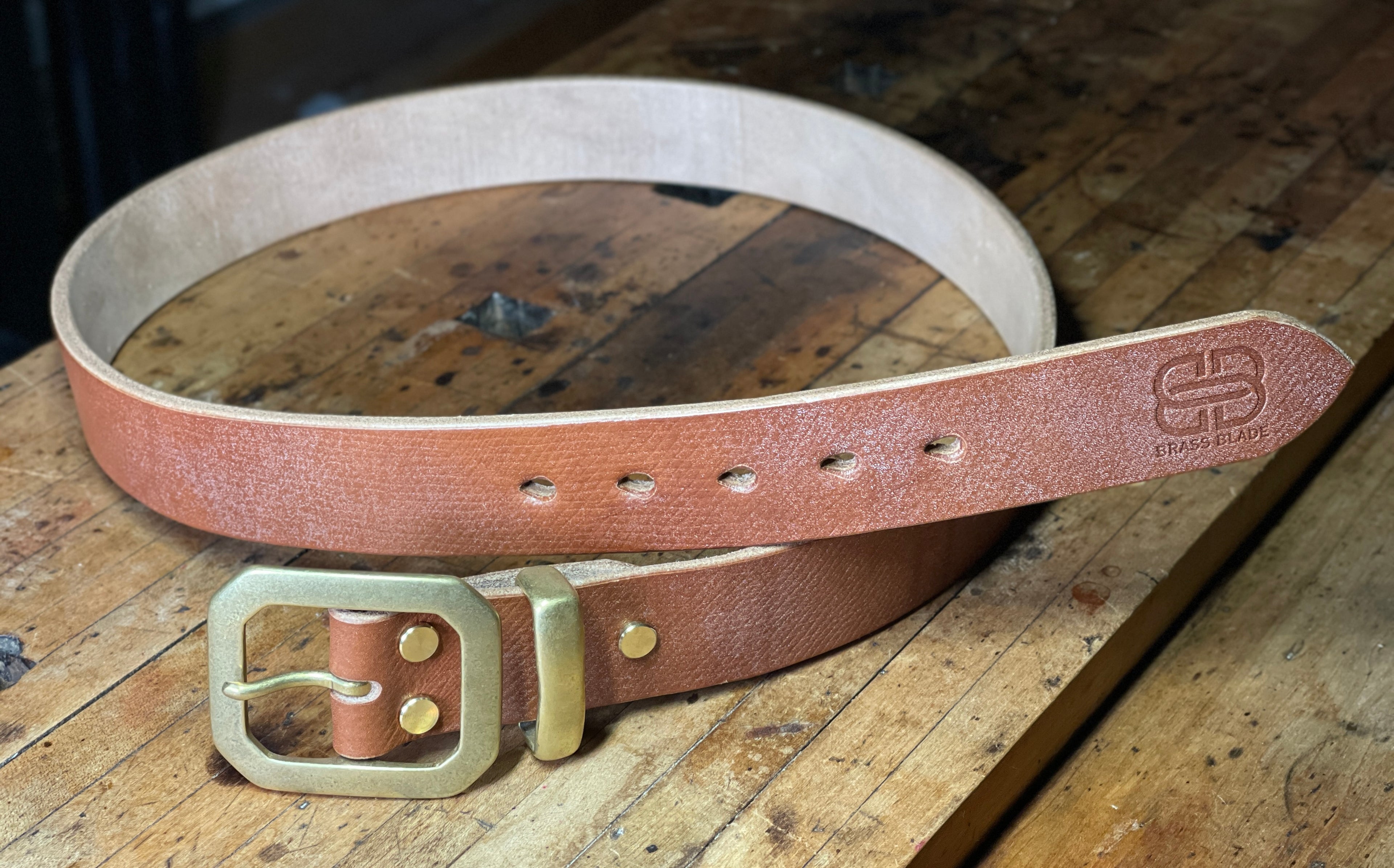 Brown leather belt with brass buckle on a wooden surface