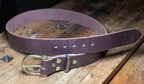 Dark brown leather belt with brass buckle on a wooden surface