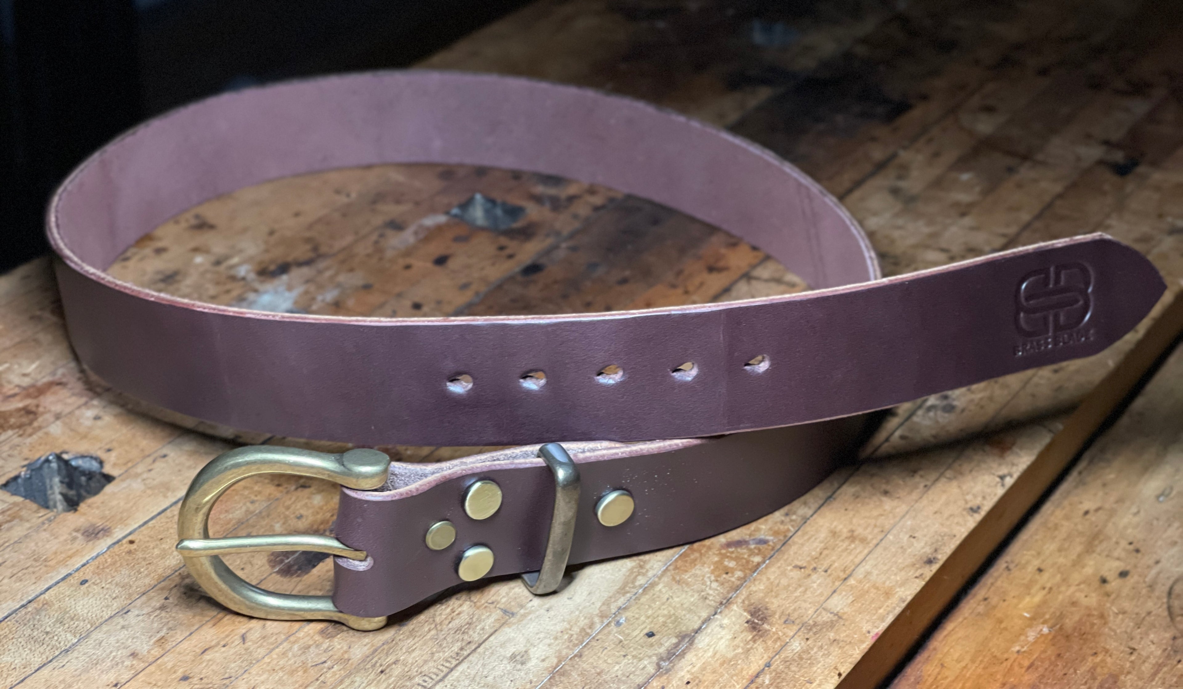 Dark brown leather belt with brass buckle on a wooden surface